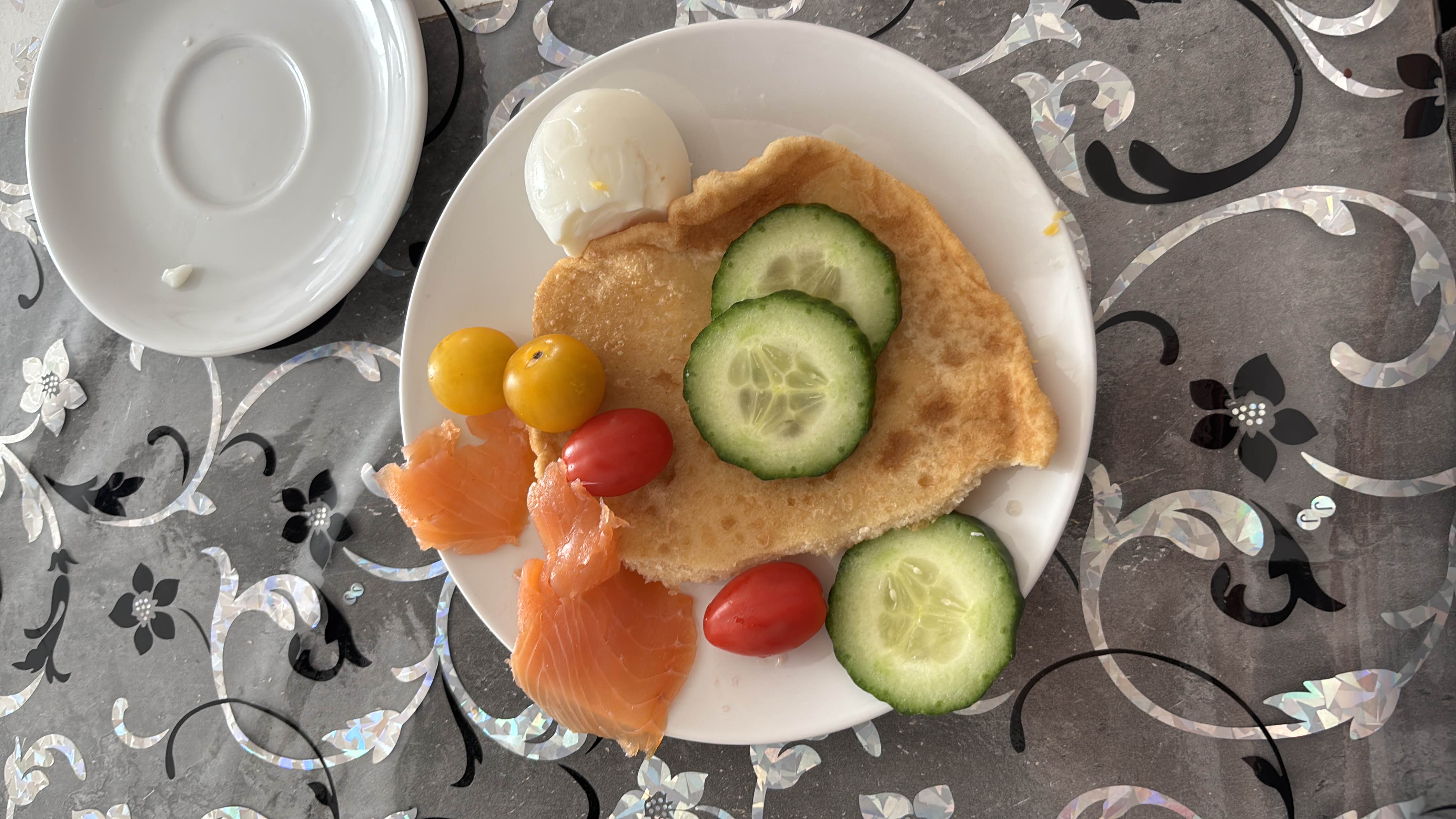 A balanced plate featuring smoked salmon, cherry tomatoes, cucumber slices, flatbread, and a boiled egg, providing a mix of protein, carbs, and healthy fats.