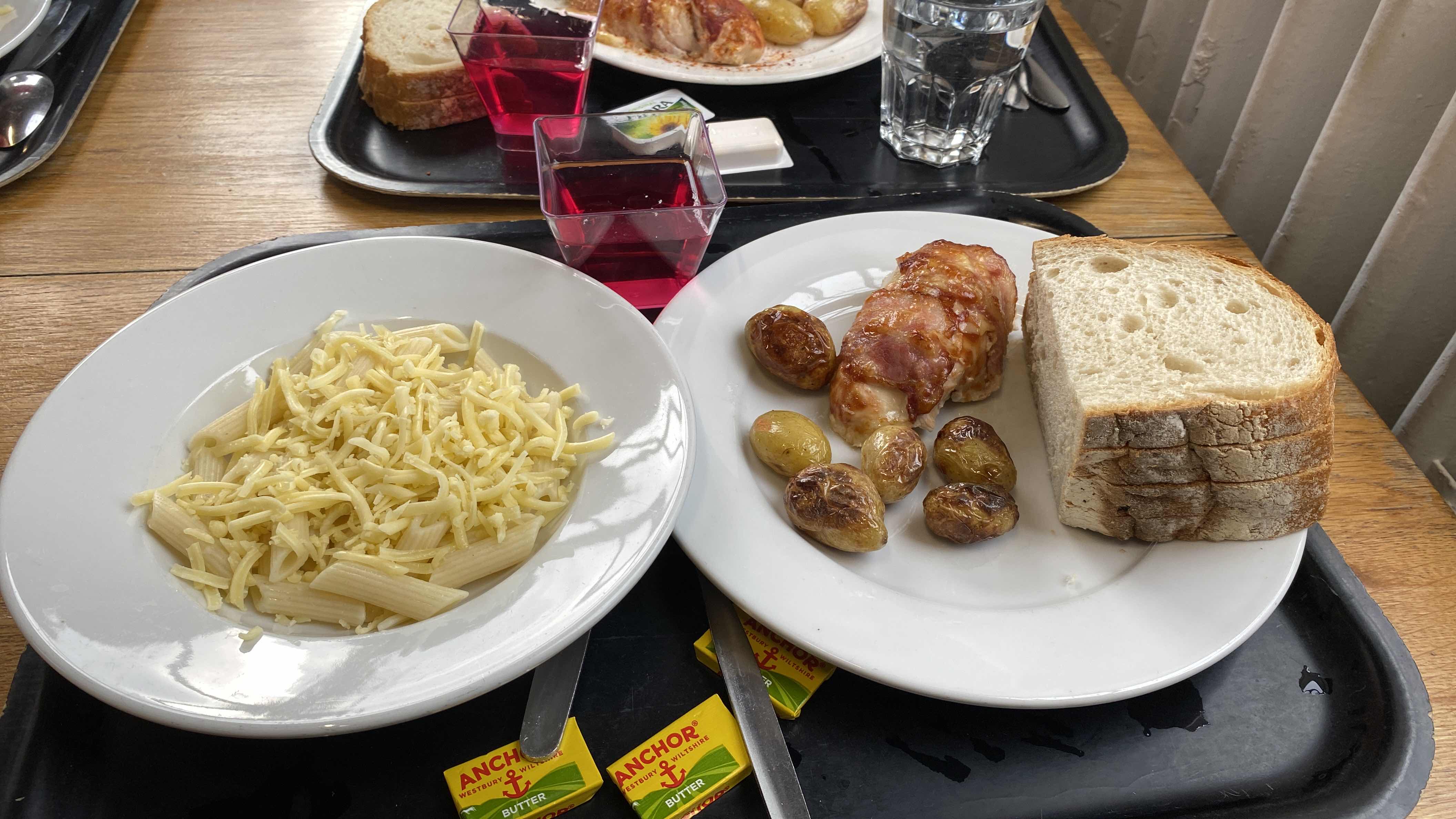A meal consisting of pasta with cheese, roasted potatoes, chicken wrapped in bacon, and bread slices.
