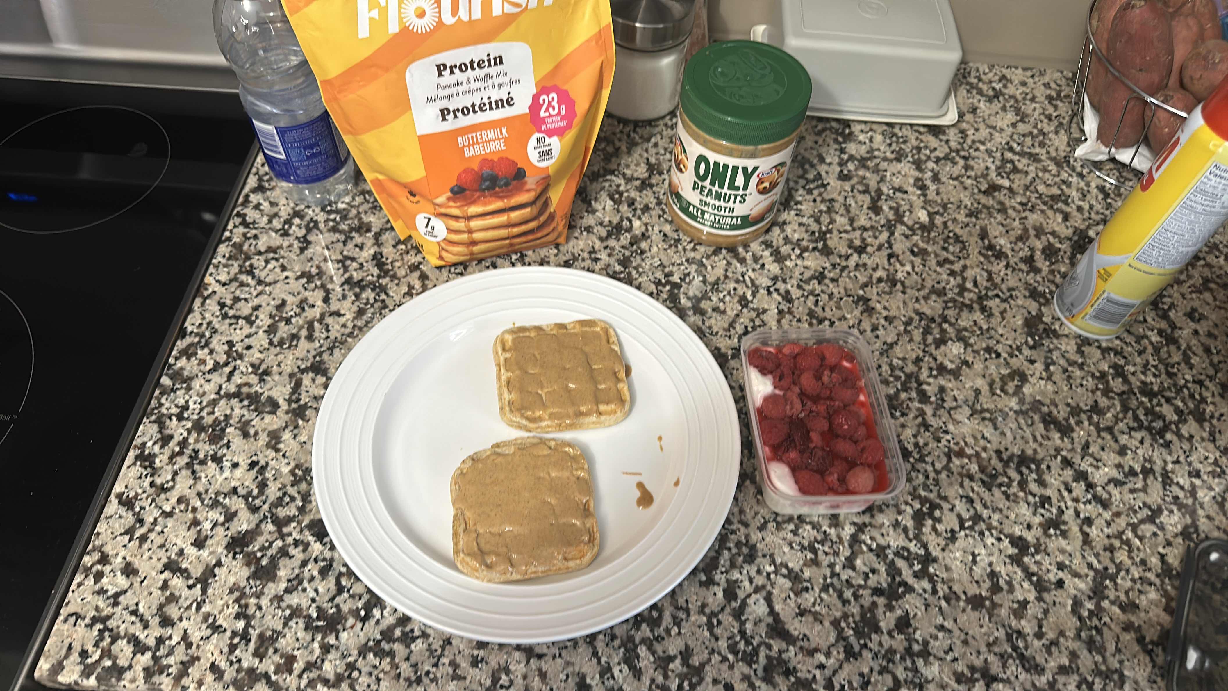 A balanced meal consisting of protein waffles topped with peanut butter and a side of raspberries, providing a good mix of protein, carbs, and fats.