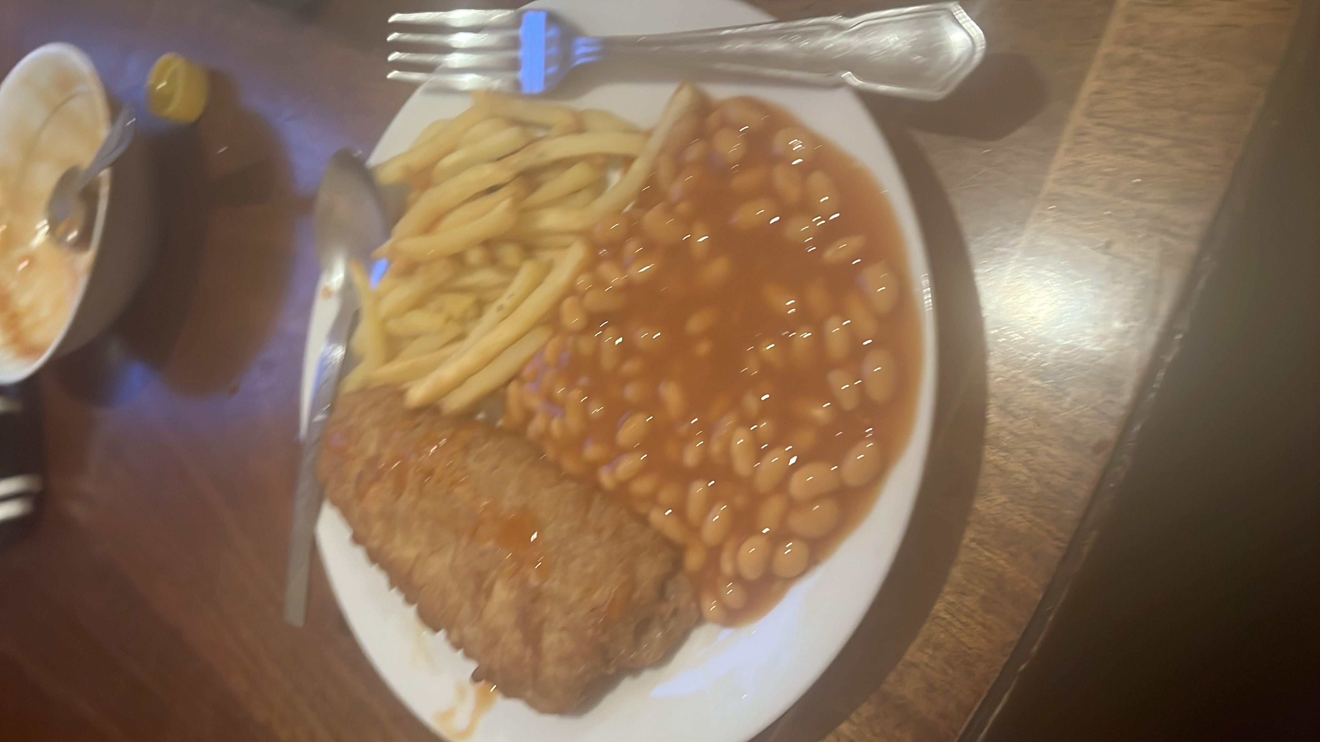 A plate containing baked beans, fries, and a fried sausage, providing a balanced mix of protein, carbs, and fats.