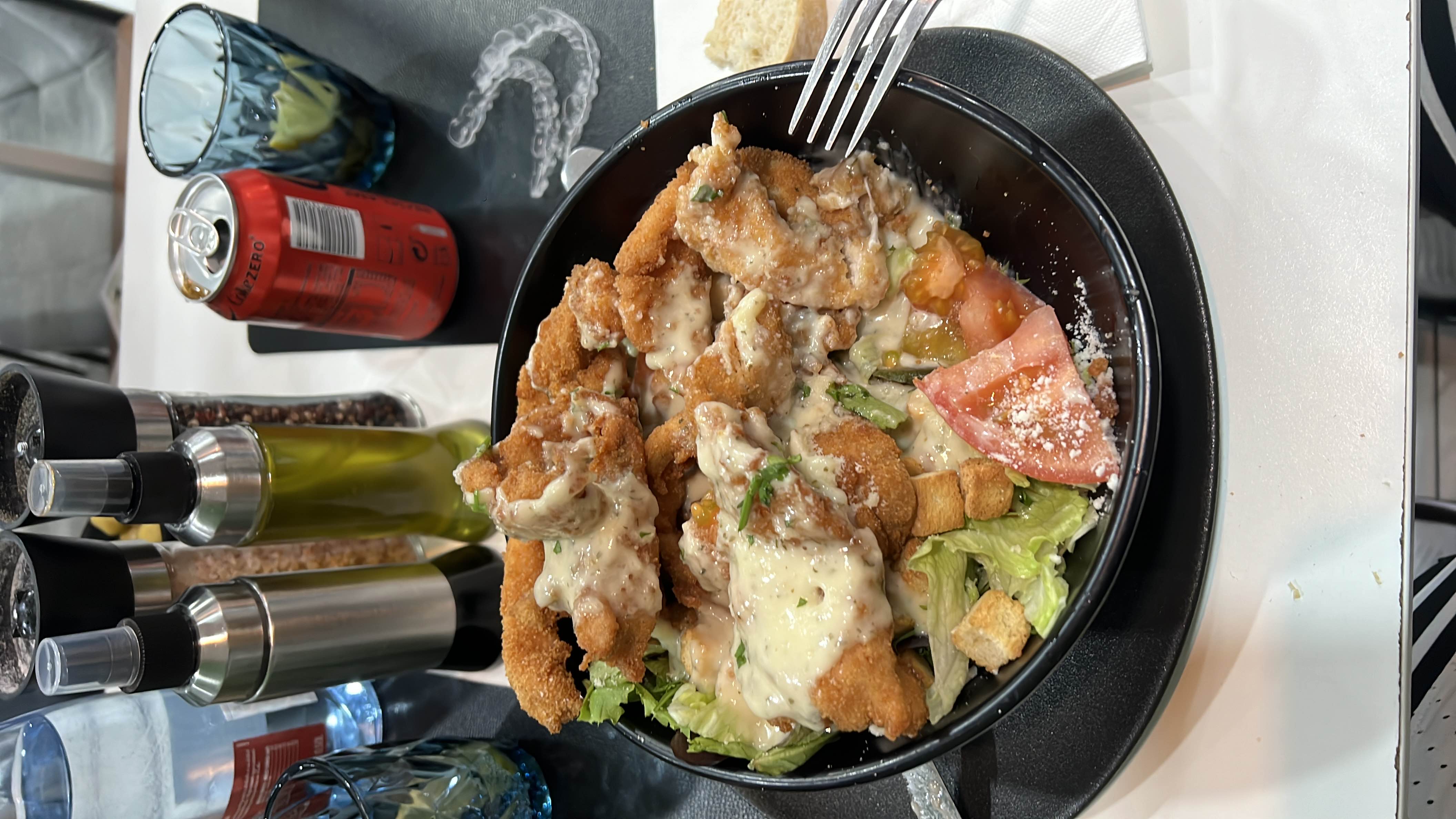 A salad bowl containing fried chicken, lettuce, tomato, croutons, and dressing, offering a balanced mix of protein, carbs, and fats.
