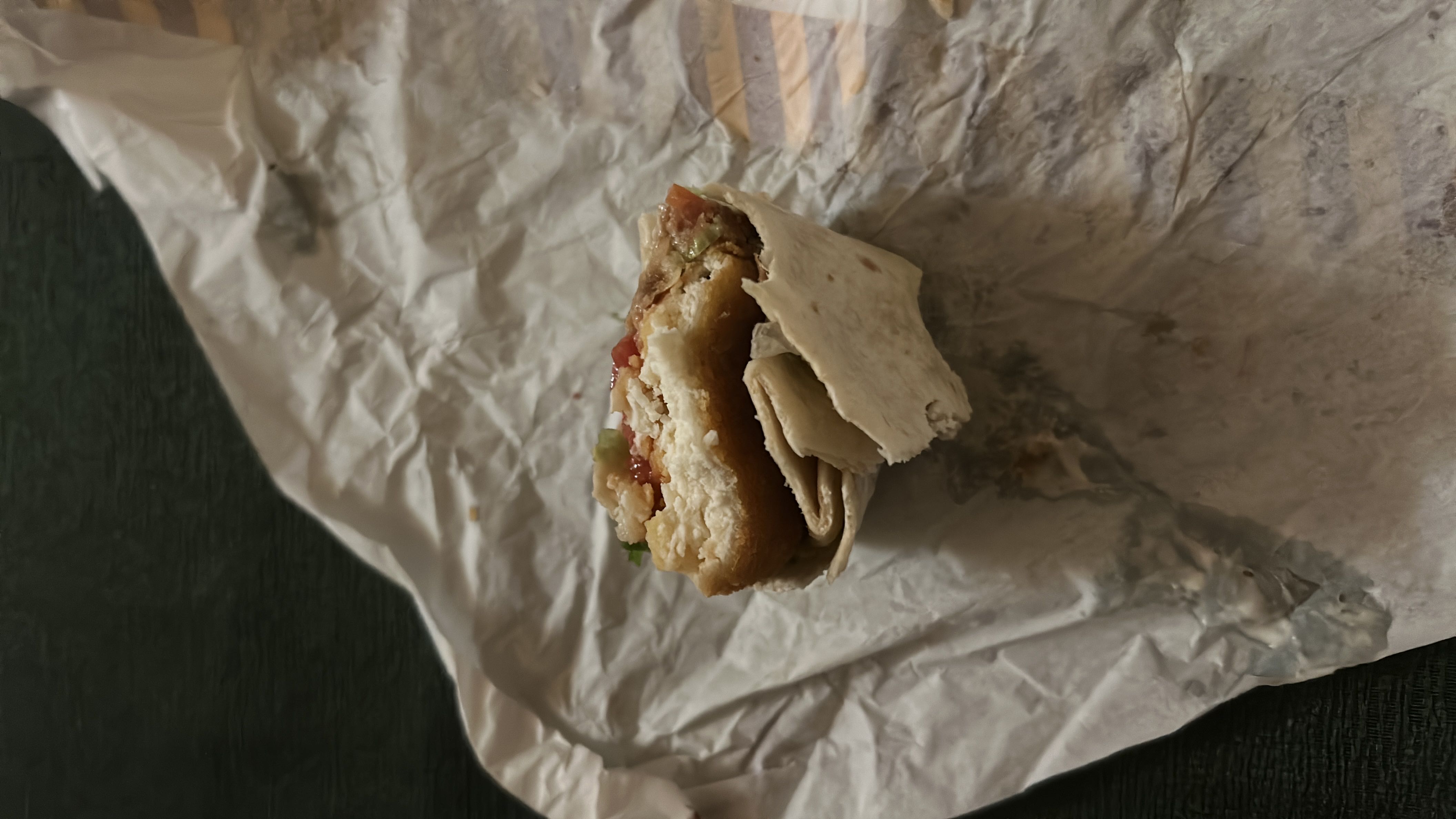 A partially eaten wrap containing chicken, vegetables, and sauce in a tortilla.