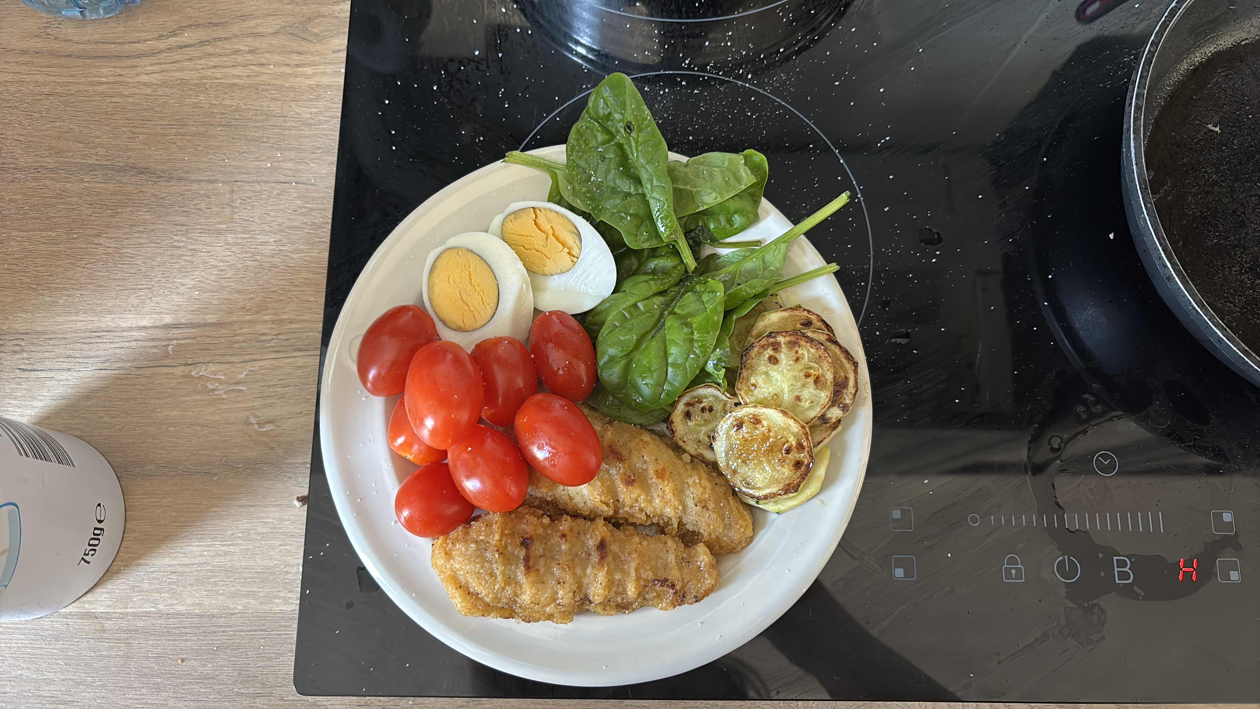A balanced meal consisting of chicken strips, cherry tomatoes, boiled egg, spinach, and grilled zucchini, providing a good mix of protein, carbs, and fats.