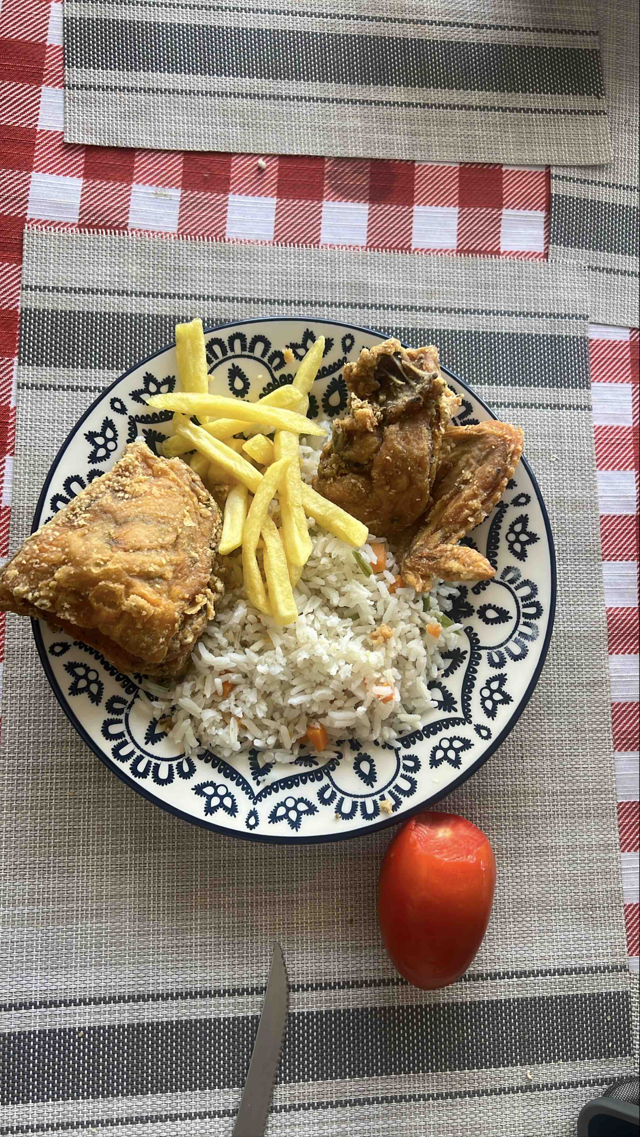 A meal consisting of fried chicken, rice with vegetables, French fries, and a fresh tomato.