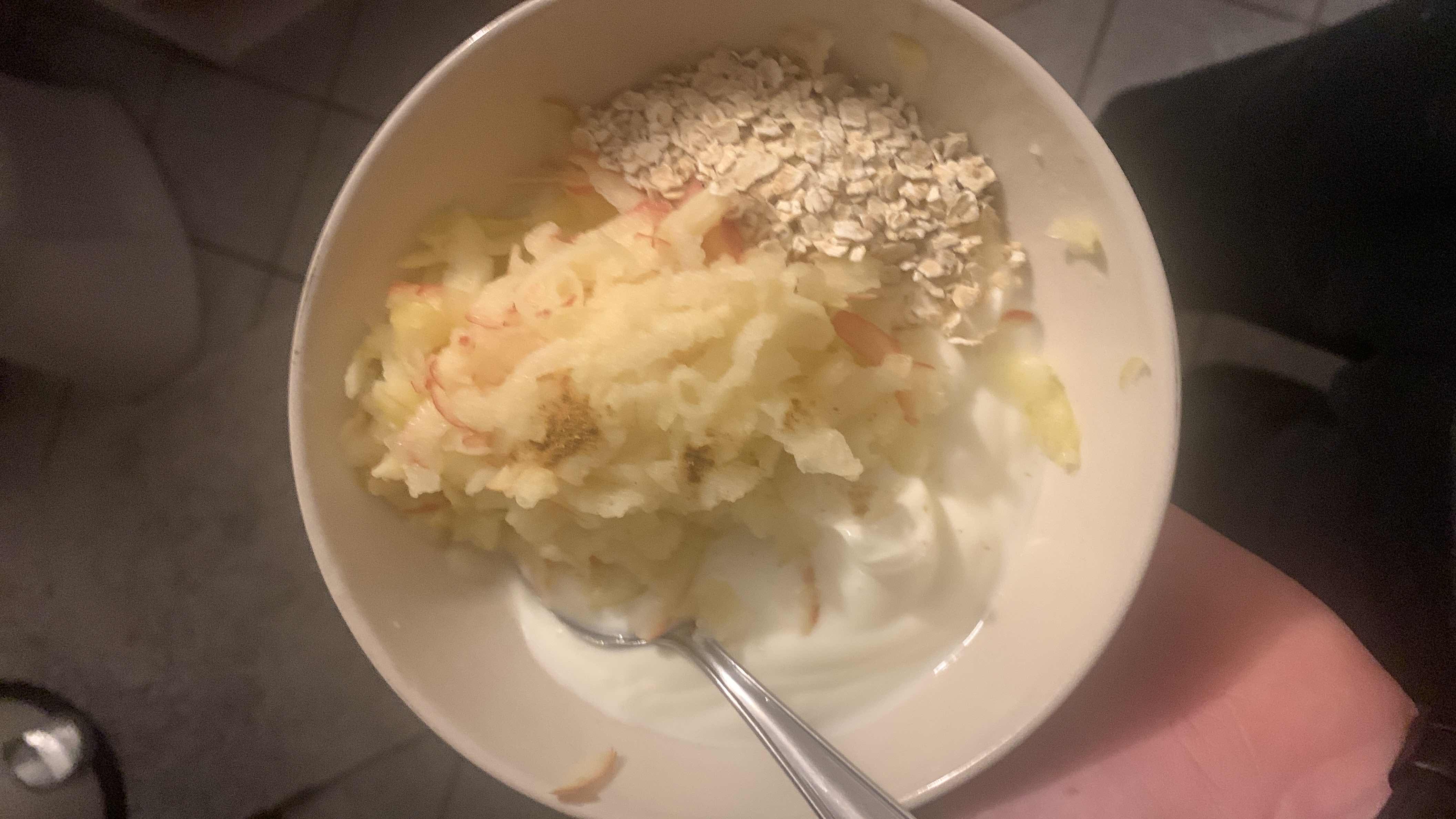 A healthy bowl containing yogurt, grated apple, and oats, providing a balanced mix of protein, carbs, and fats.