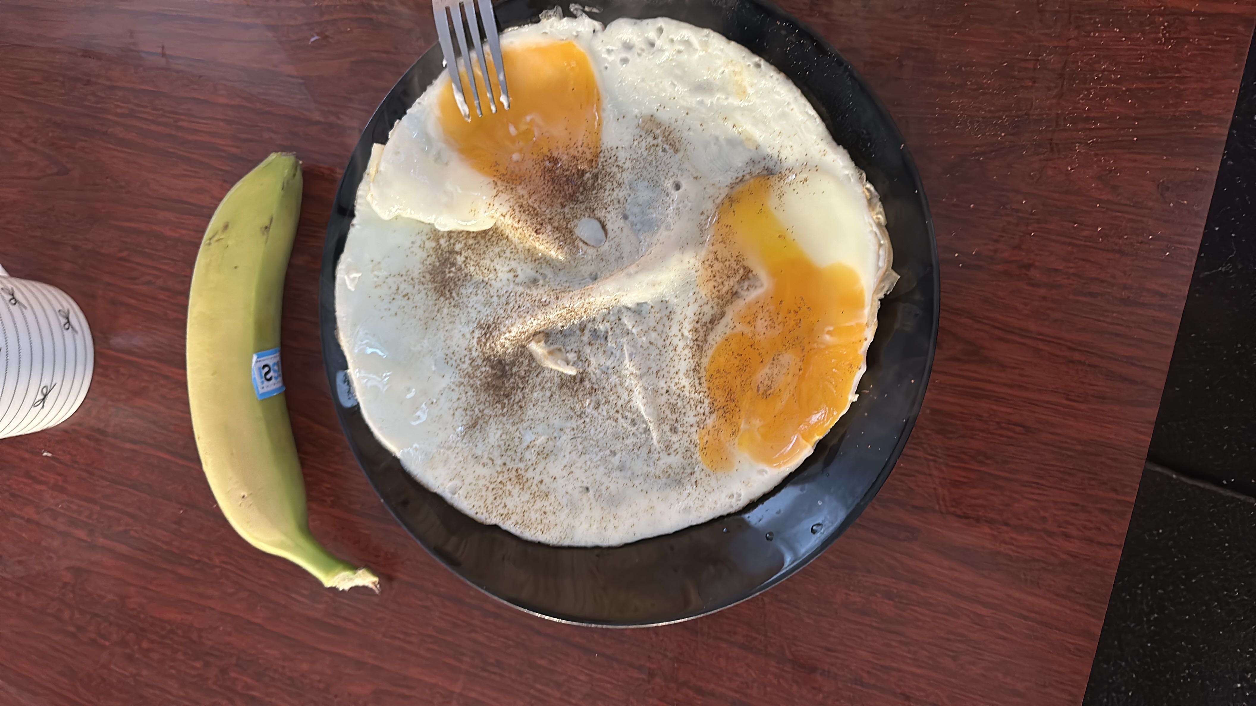 A plate of two fried eggs seasoned with pepper, accompanied by a banana, providing a balanced mix of protein, carbs, and fats.