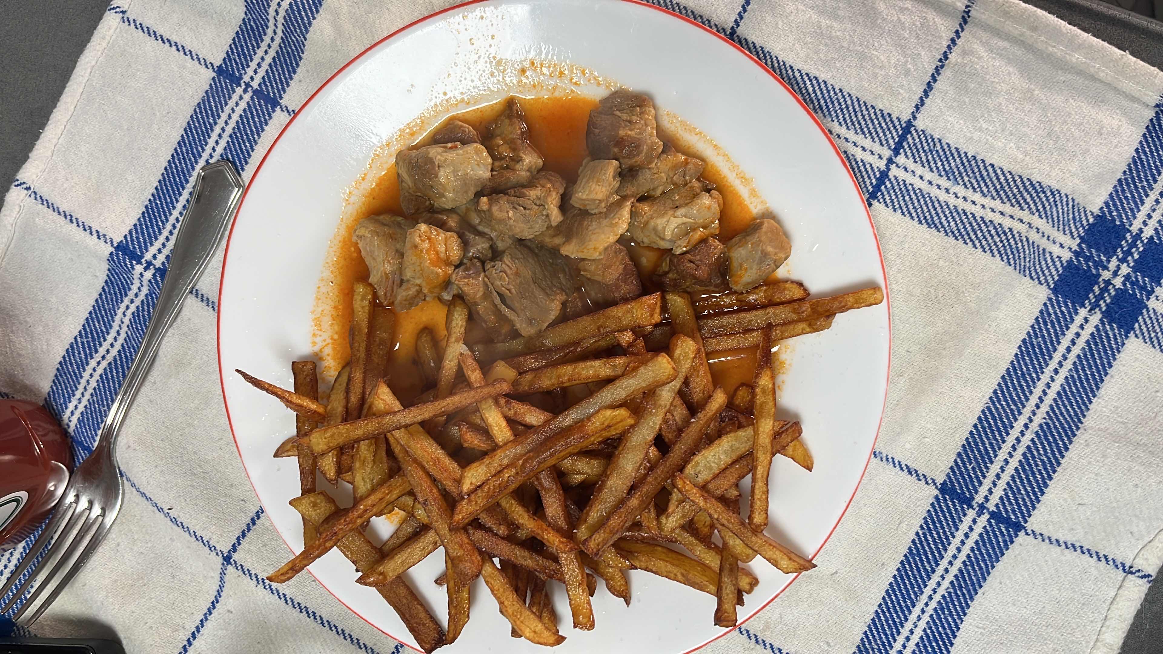 A dish consisting of beef chunks in tomato sauce served with fried potatoes.