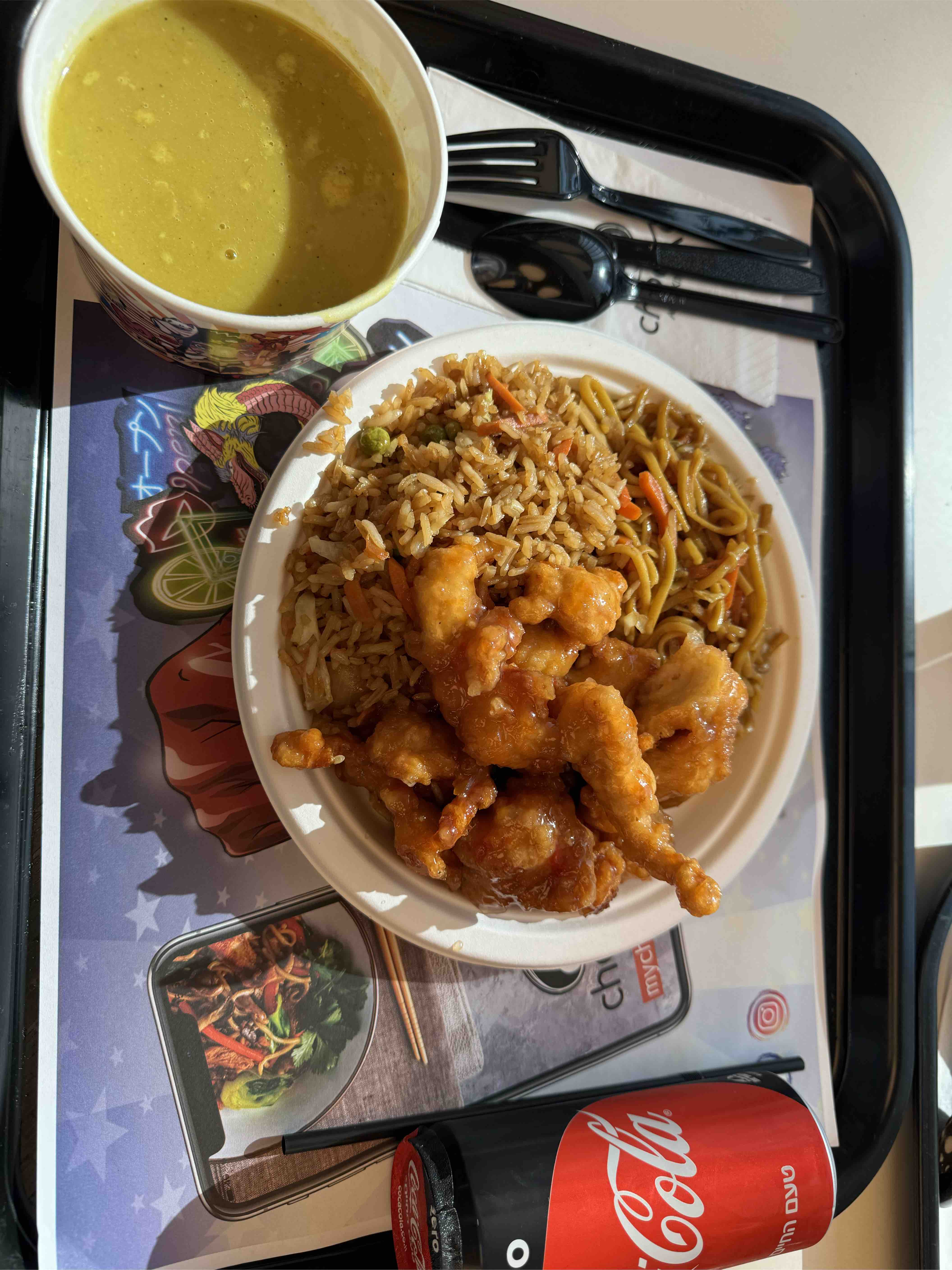 A meal consisting of fried rice, noodles, fried chicken, soup, and a soda, providing a moderate balance of protein, carbs, and fats.