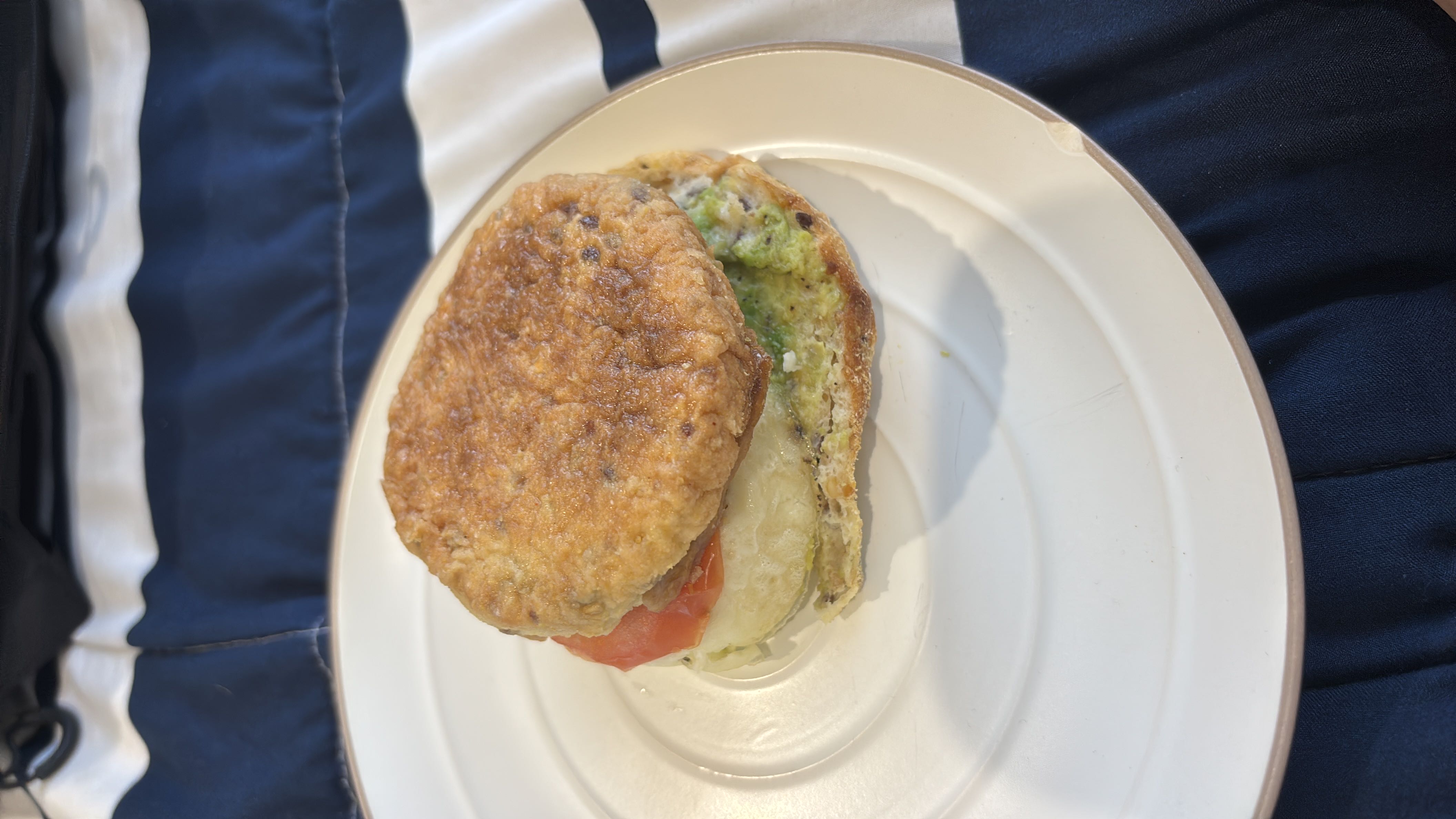 A sandwich made with an egg patty, tomato slice, cheese, avocado spread, and a whole grain bun, providing a balanced mix of protein, carbs, and fats.