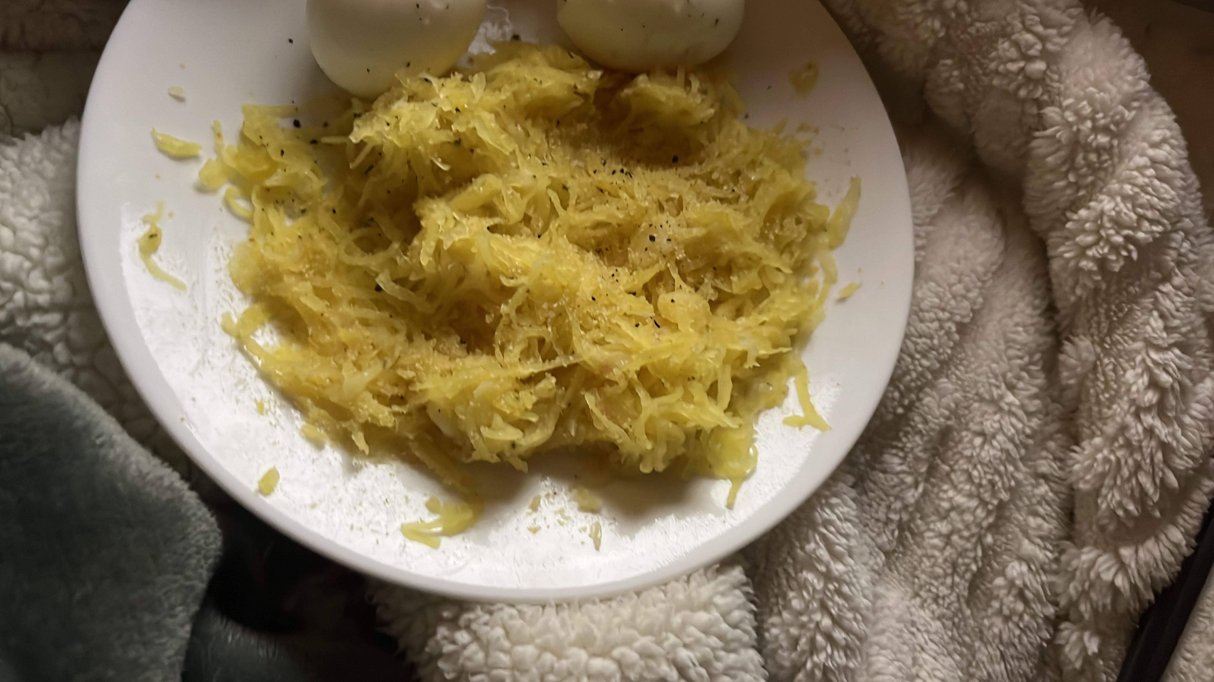 A plate containing spaghetti squash seasoned with pepper and a boiled egg, offering a low-calorie, protein-rich meal.