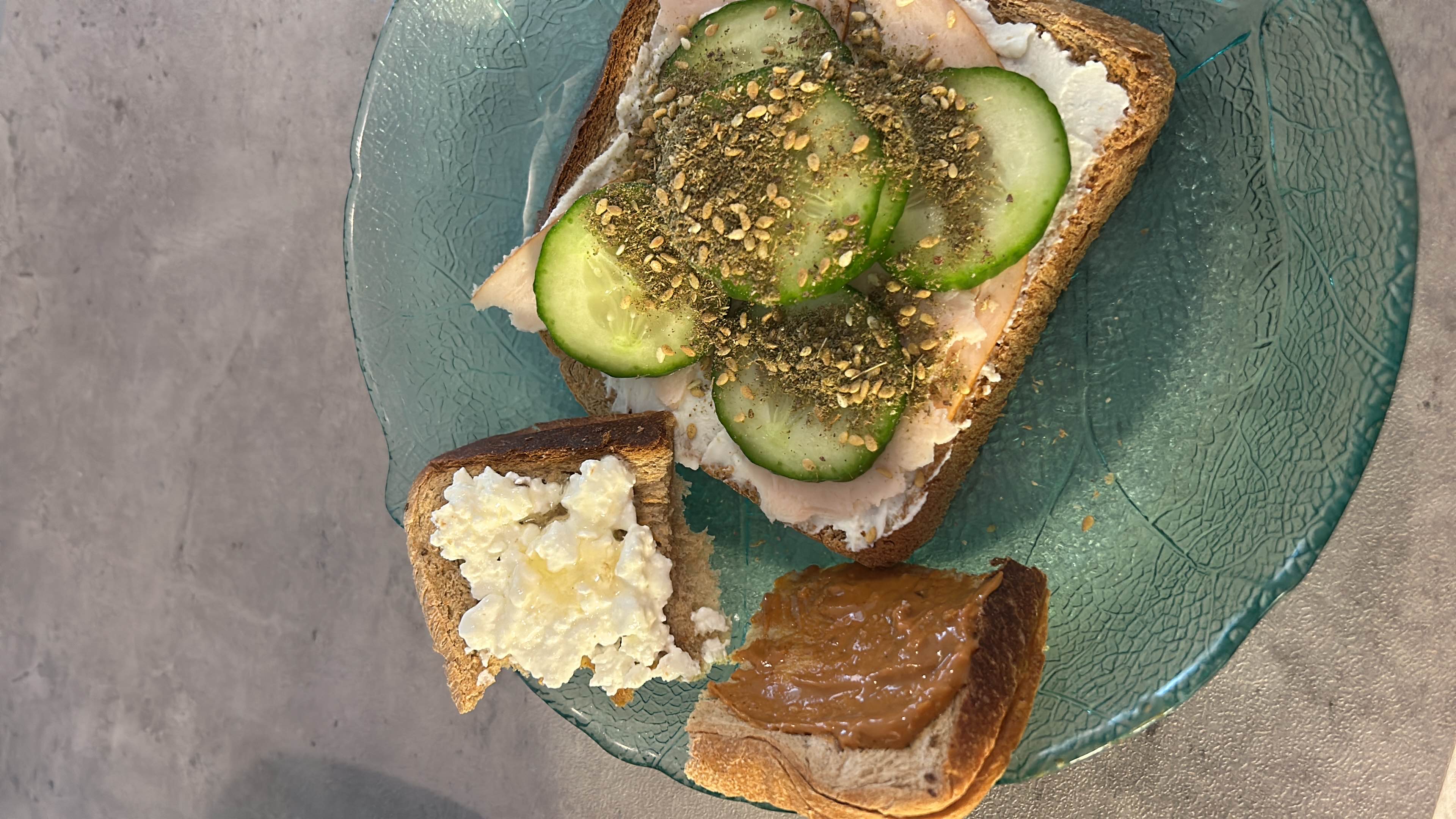 A balanced, high-protein meal featuring High protein pain demi from Carrefour topped with cottage cheese, peanut butter, turkey slices, cucumber slices, and za'atar seasoning.
