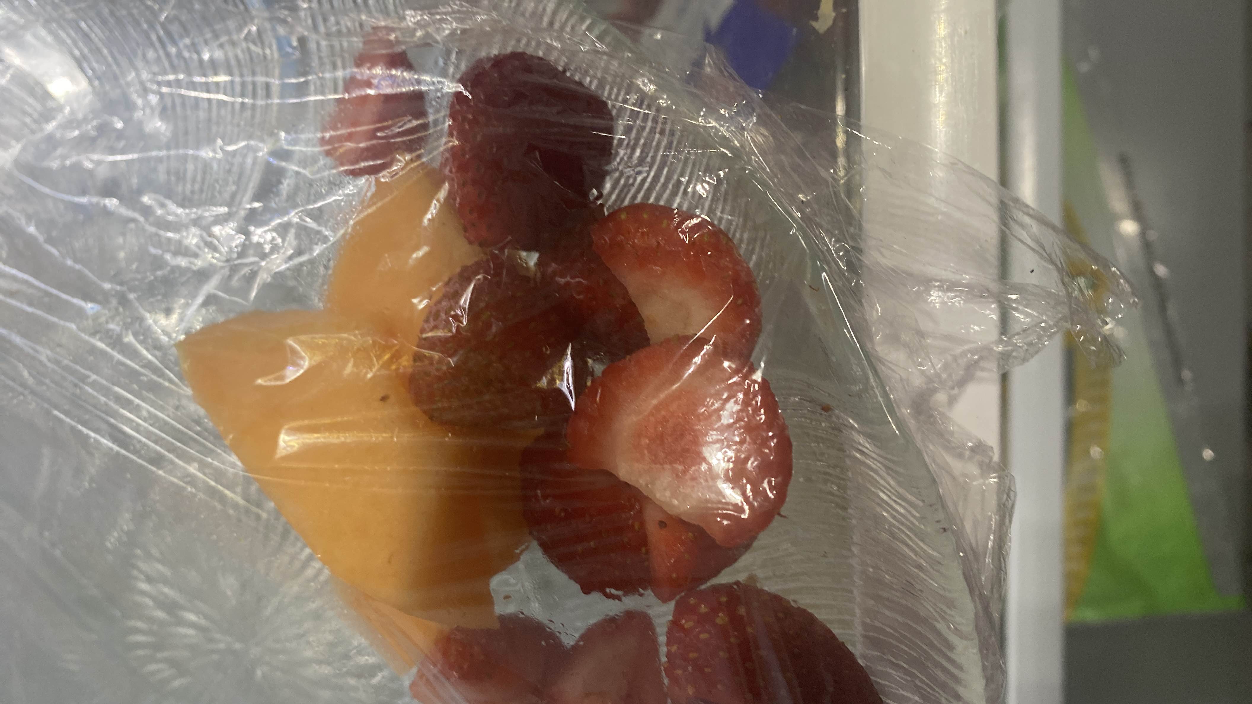 The image shows a mix of fresh strawberries and cantaloupe slices wrapped in plastic, providing a low-calorie, nutrient-rich snack.