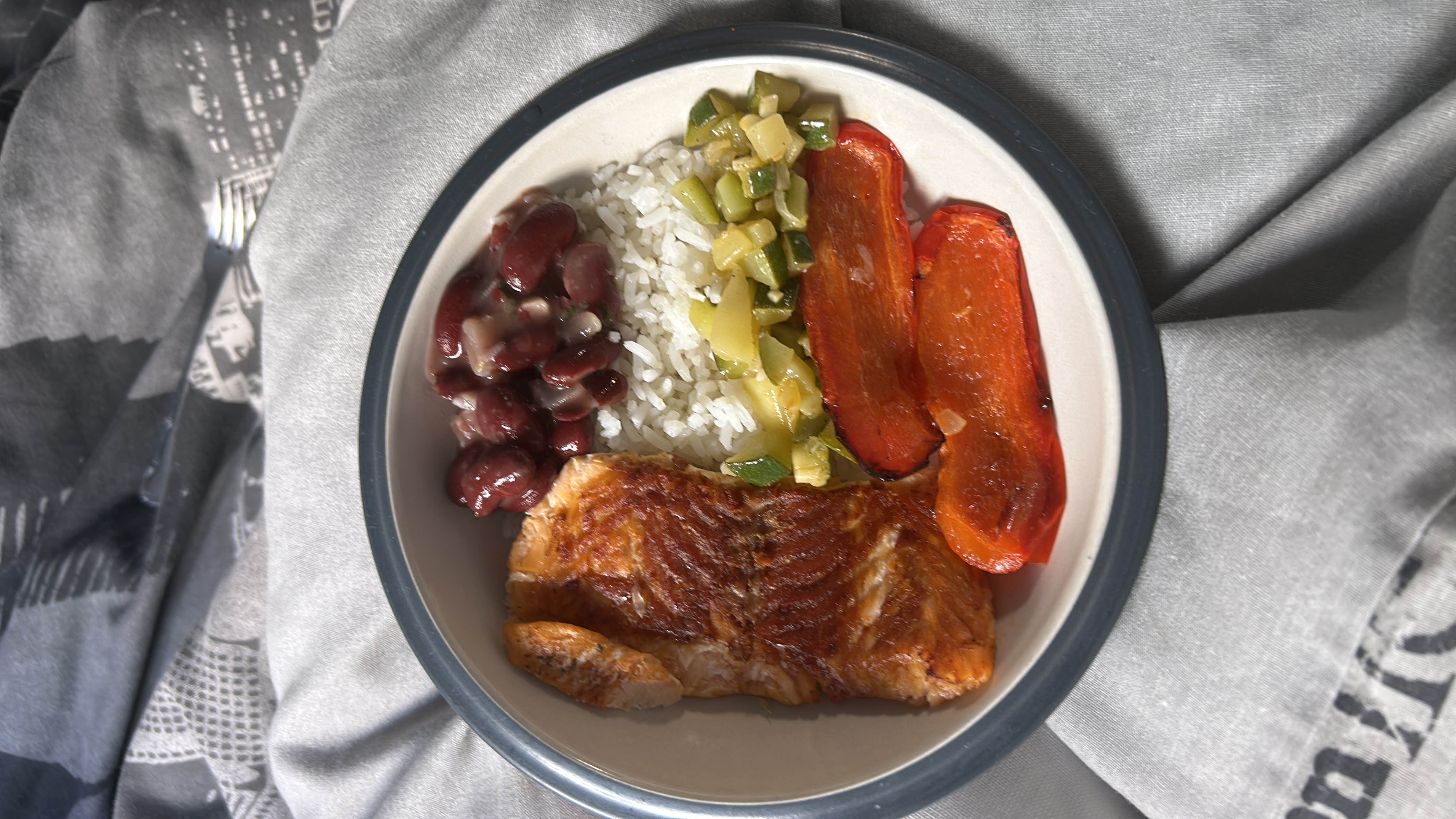 A balanced meal consisting of grilled salmon, white rice, red kidney beans, zucchini, and roasted red bell pepper, providing a good mix of protein, carbs, and healthy fats.