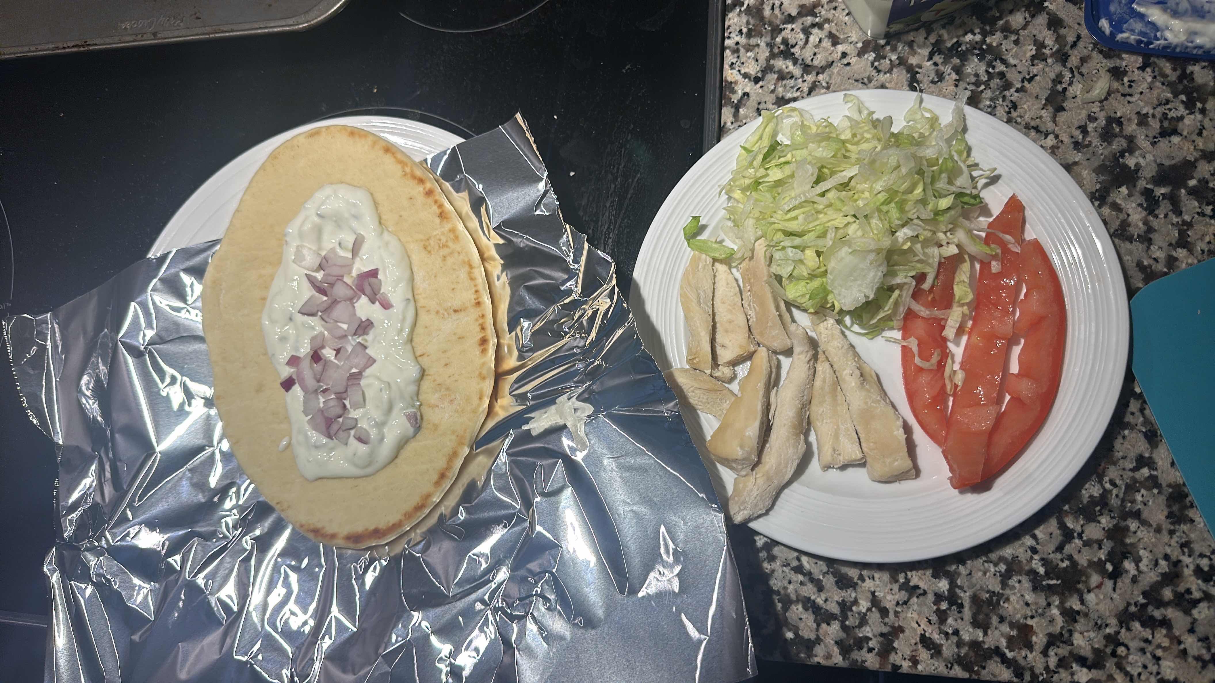A pita wrap with chicken, tzatziki sauce, red onion, lettuce, and tomato, served with fresh ingredients.