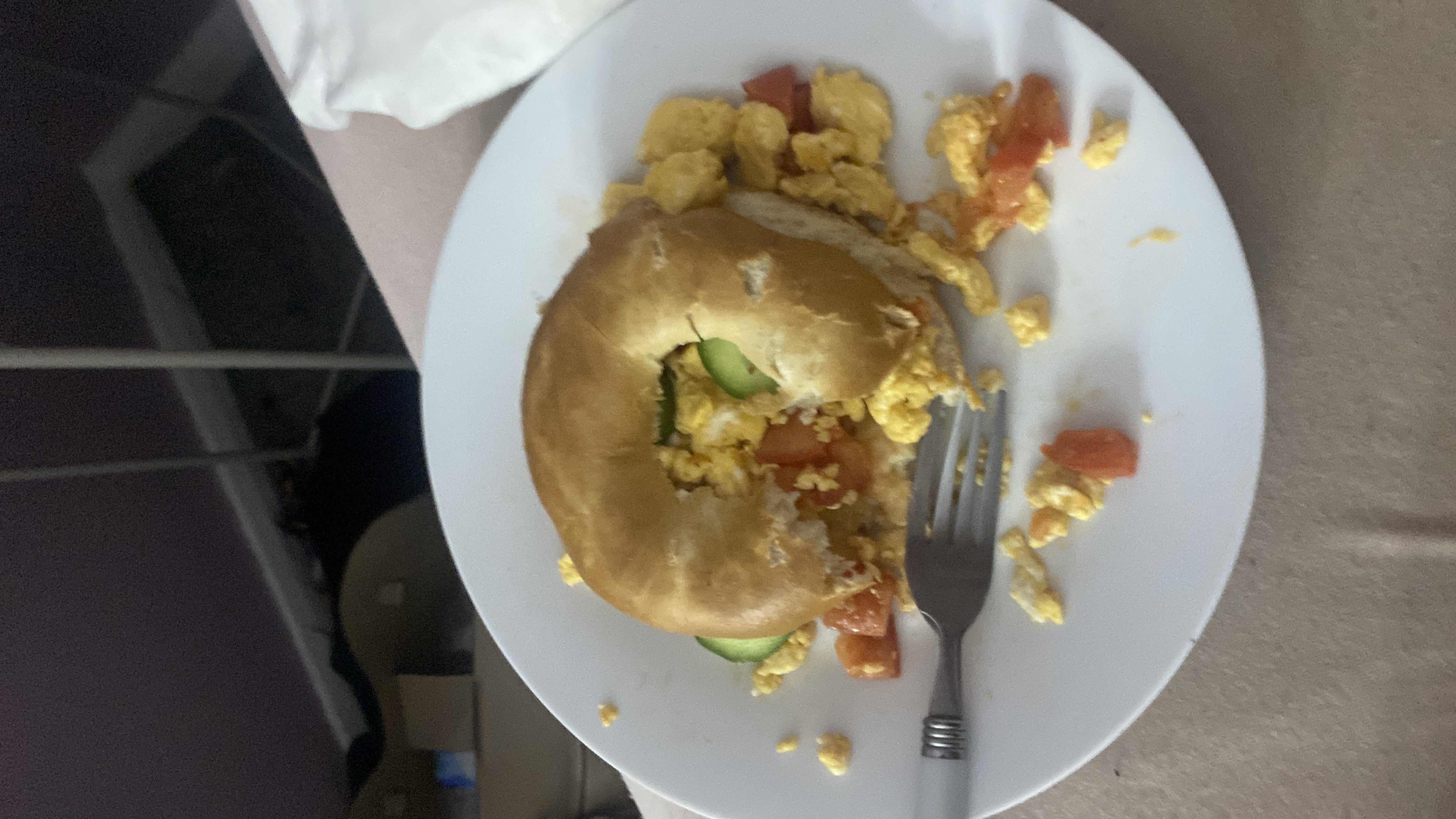 A bagel sandwich filled with scrambled eggs, tomato, and cucumber, providing a balanced mix of carbs, protein, and fats.