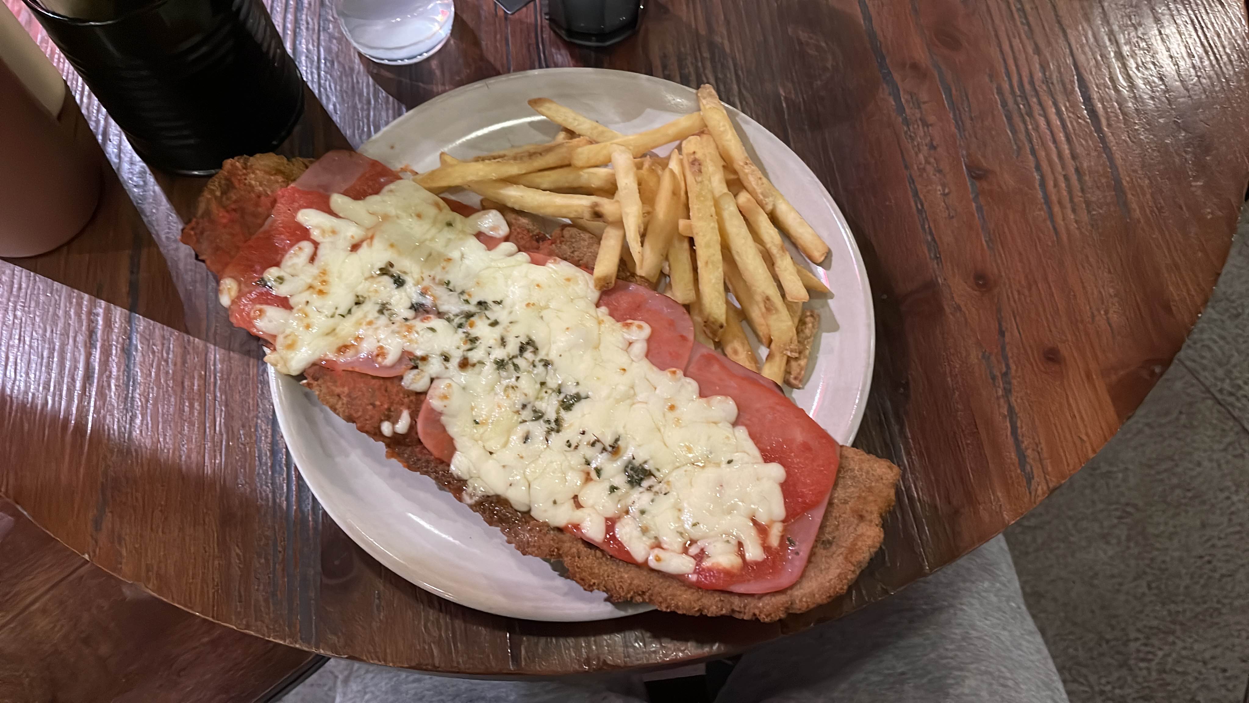 A dish consisting of breaded meat topped with ham, cheese, and tomato sauce, served with a side of fries.