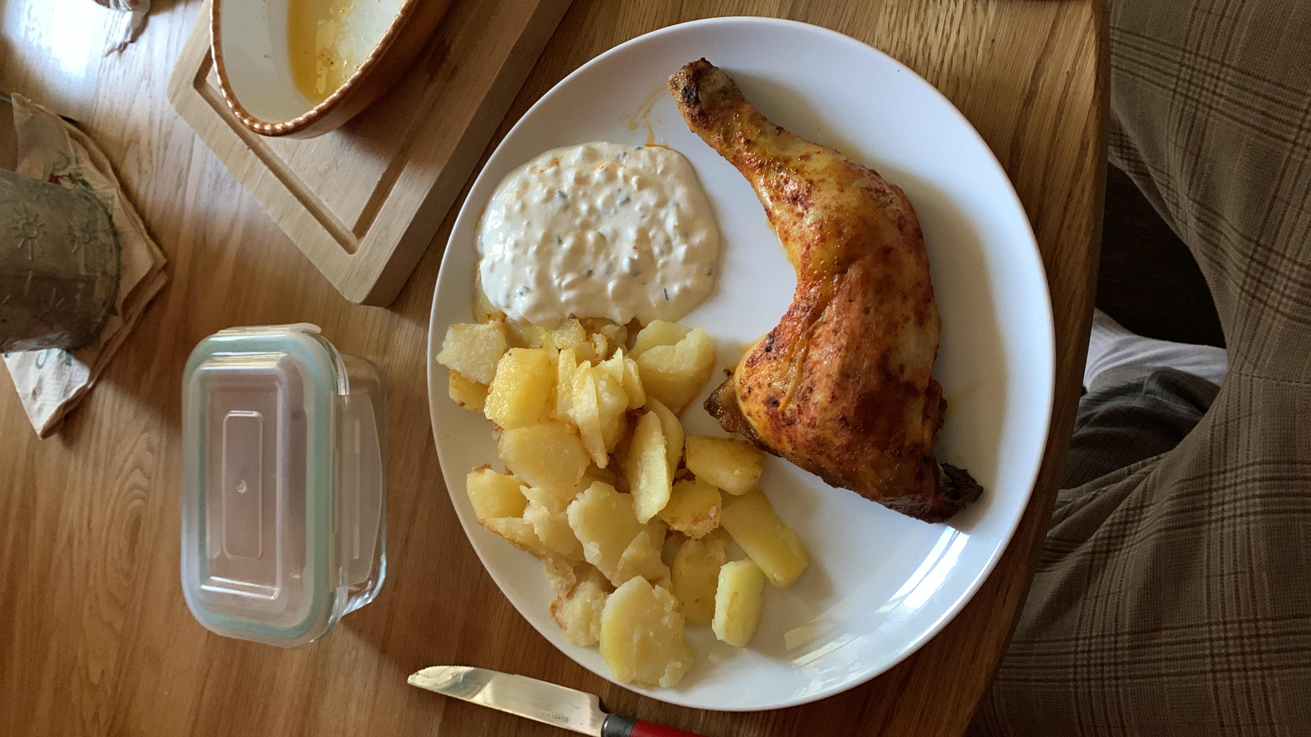 A meal consisting of a roasted chicken leg, roasted potatoes, and a creamy sauce.