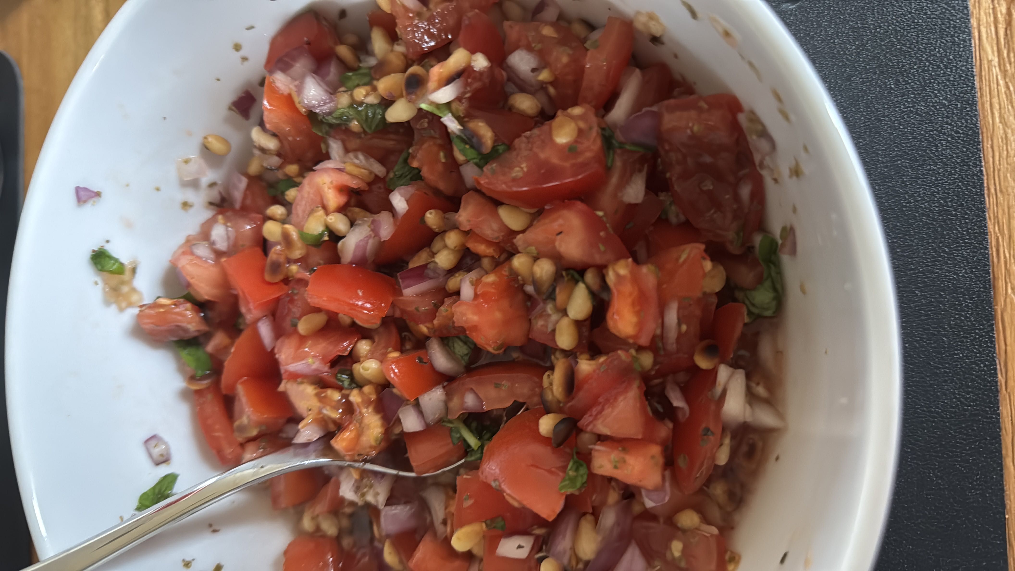 A fresh and healthy salad made with tomatoes, red onion, pine nuts, fresh herbs, and balsamic vinegar, offering a balanced mix of nutrients.
