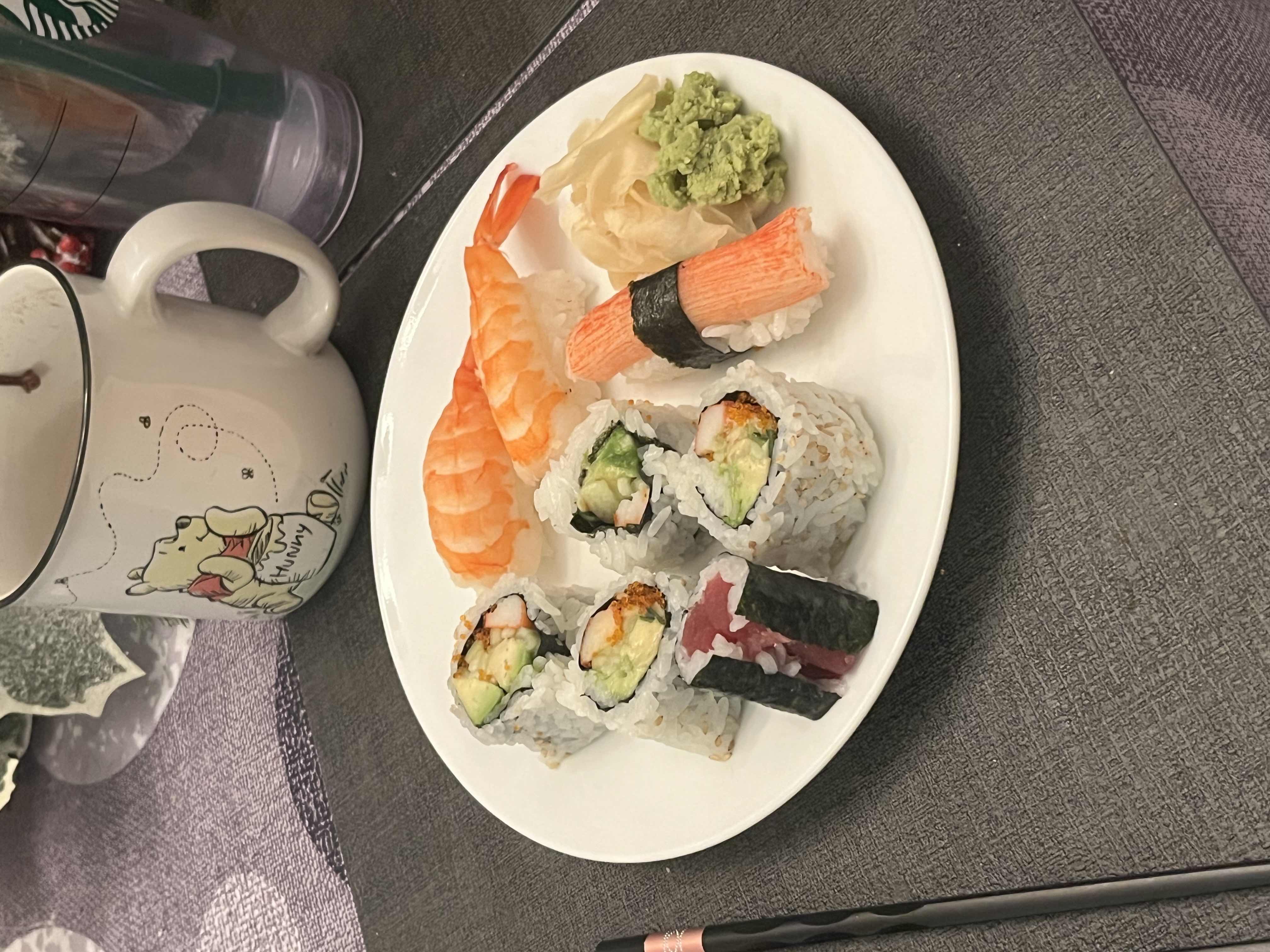 A plate of assorted sushi including rolls with avocado, crab stick, and seaweed, as well as shrimp nigiri, served with wasabi and pickled ginger.