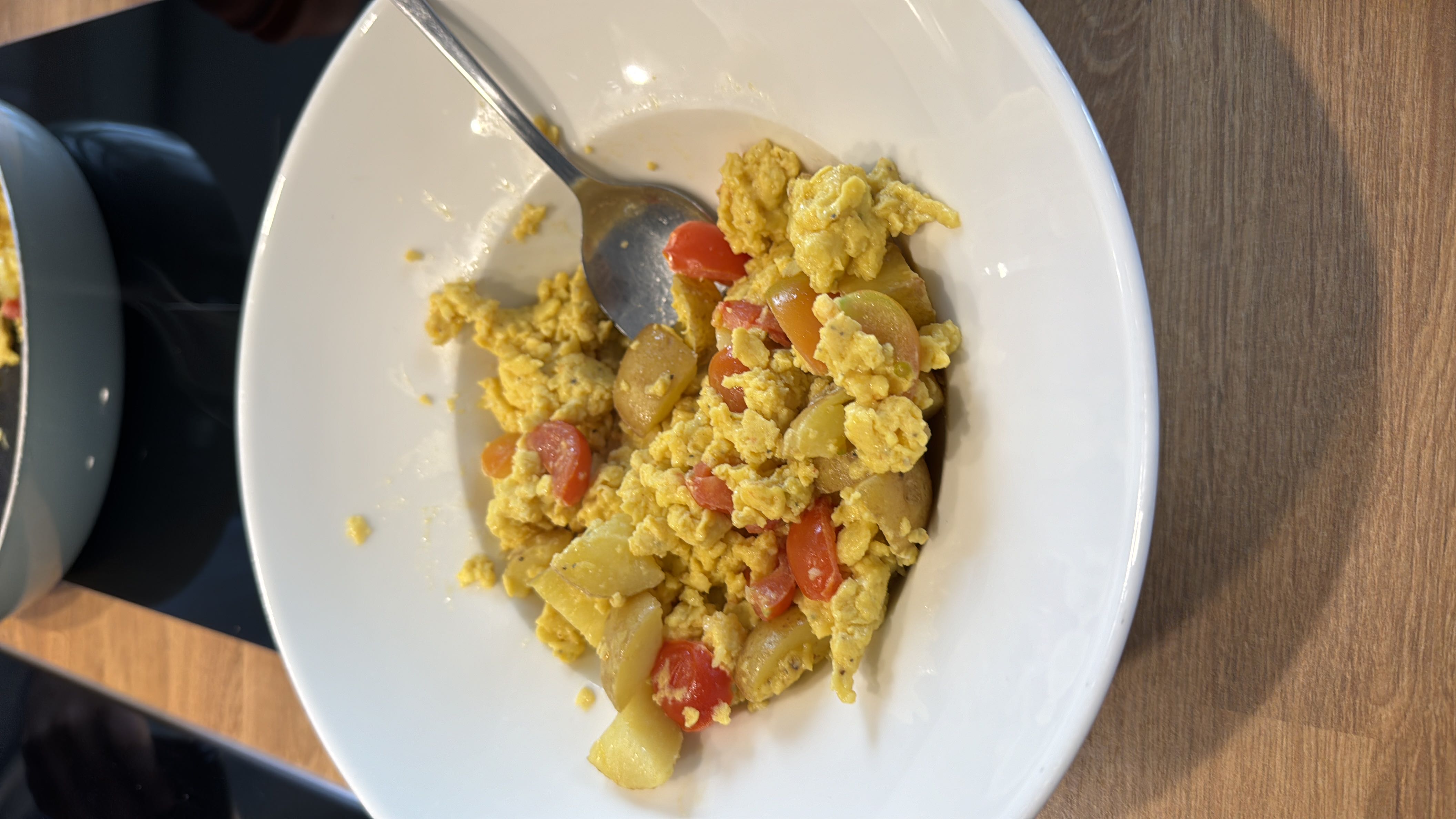 A hearty dish of scrambled eggs, potatoes, cherry tomatoes, and olive oil, offering a rich mix of protein, carbohydrates, and fats.