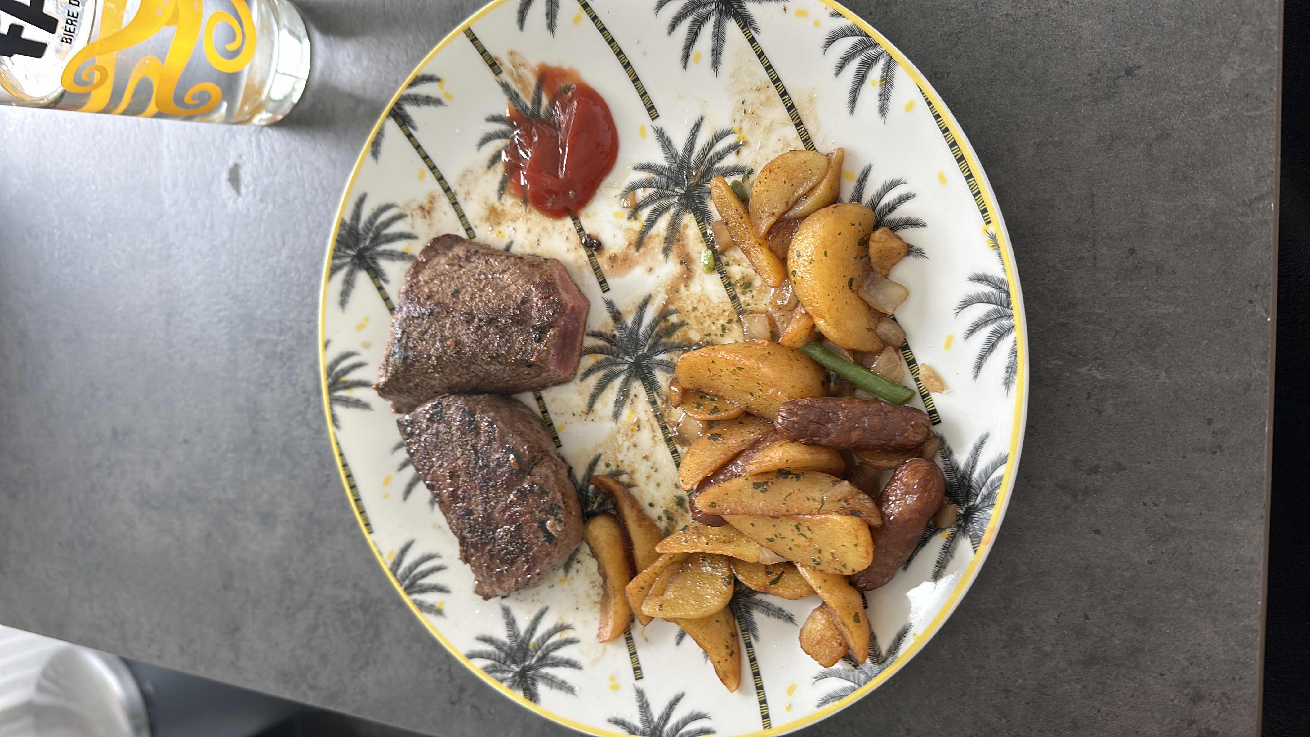 A meal consisting of grilled steak, roasted potatoes, and a side of ketchup.