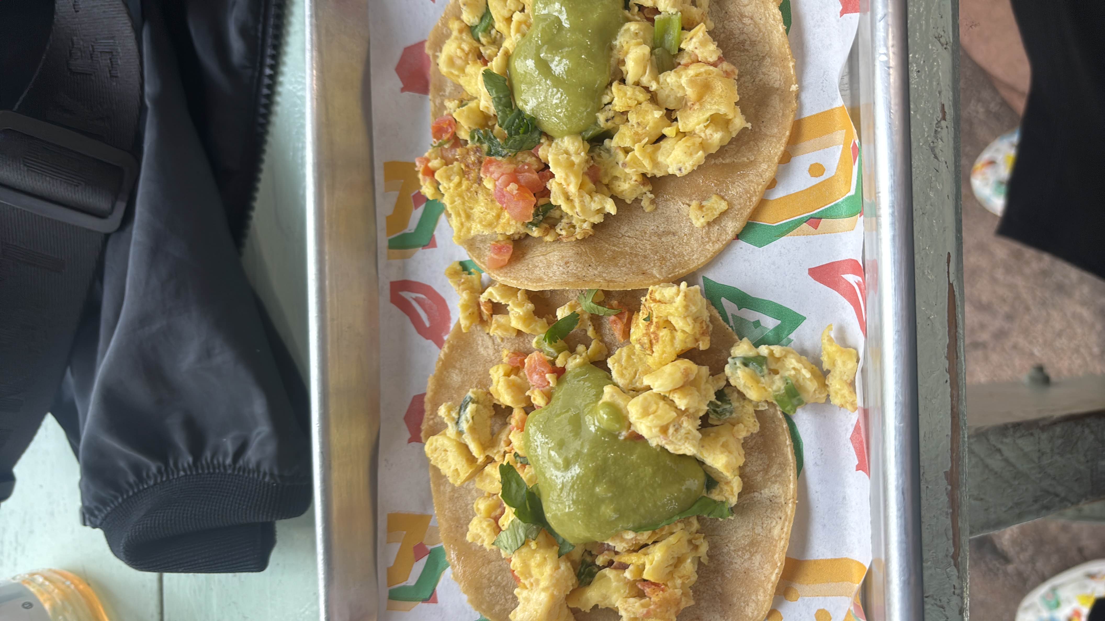 Two tacos with scrambled eggs, guacamole, and fresh herbs served on corn tortillas.