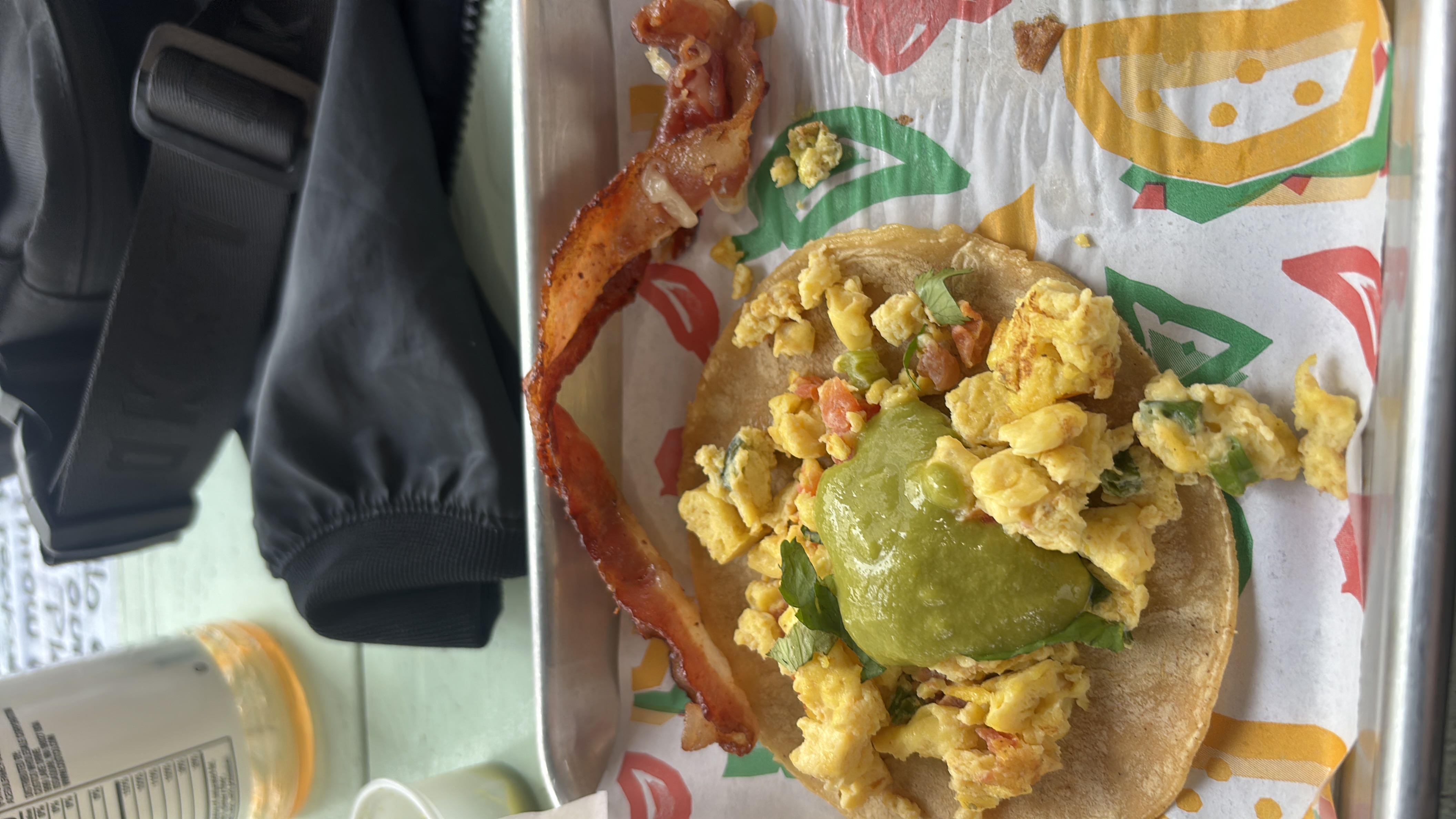 A breakfast taco with scrambled eggs, guacamole, bacon, and a corn tortilla.