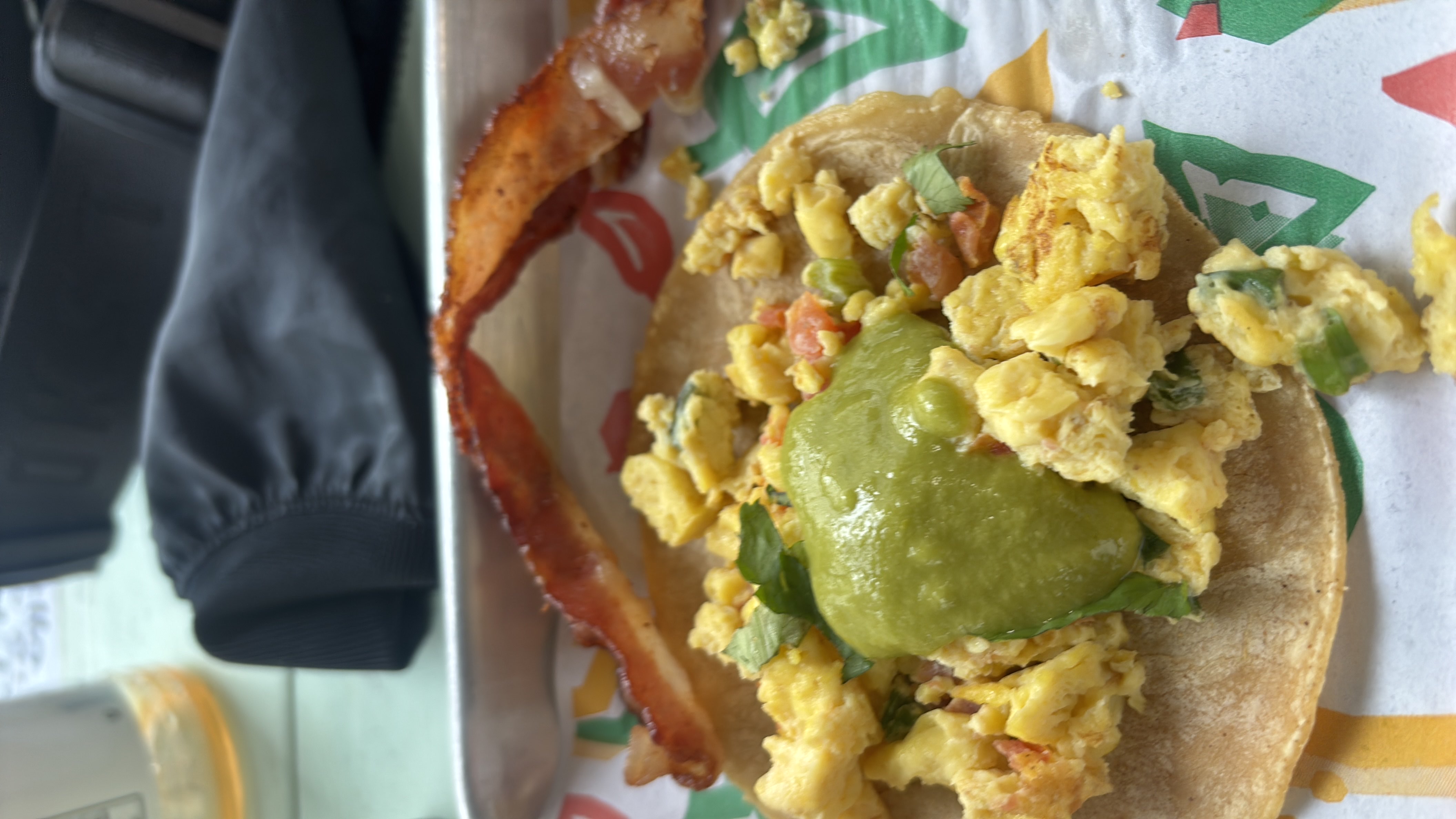 A breakfast taco with scrambled eggs, guacamole, and bacon served on a corn tortilla.