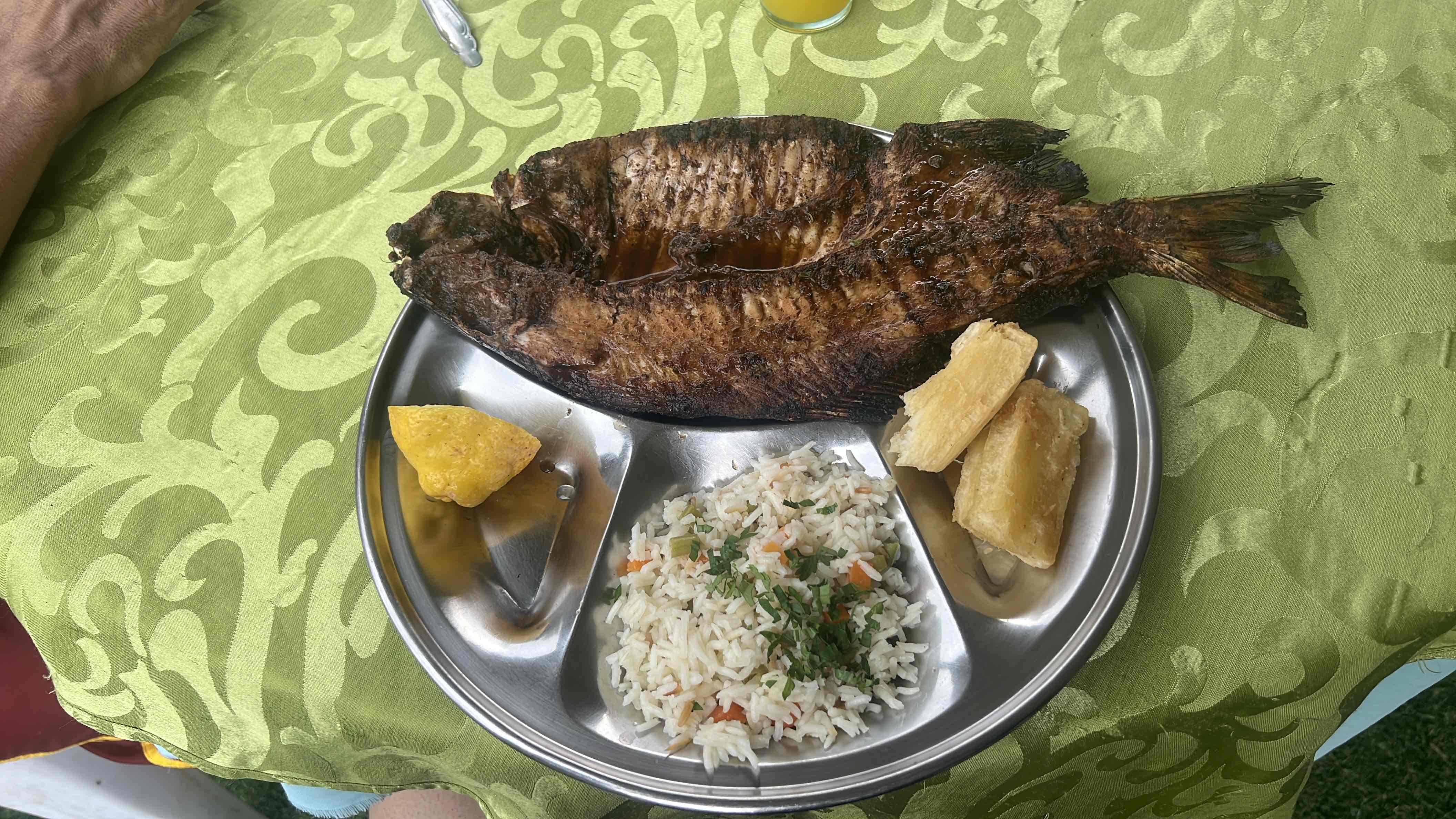 A balanced meal consisting of grilled fish, rice with vegetables, cassava, and fried plantain, providing a good mix of protein, carbs, and fats.