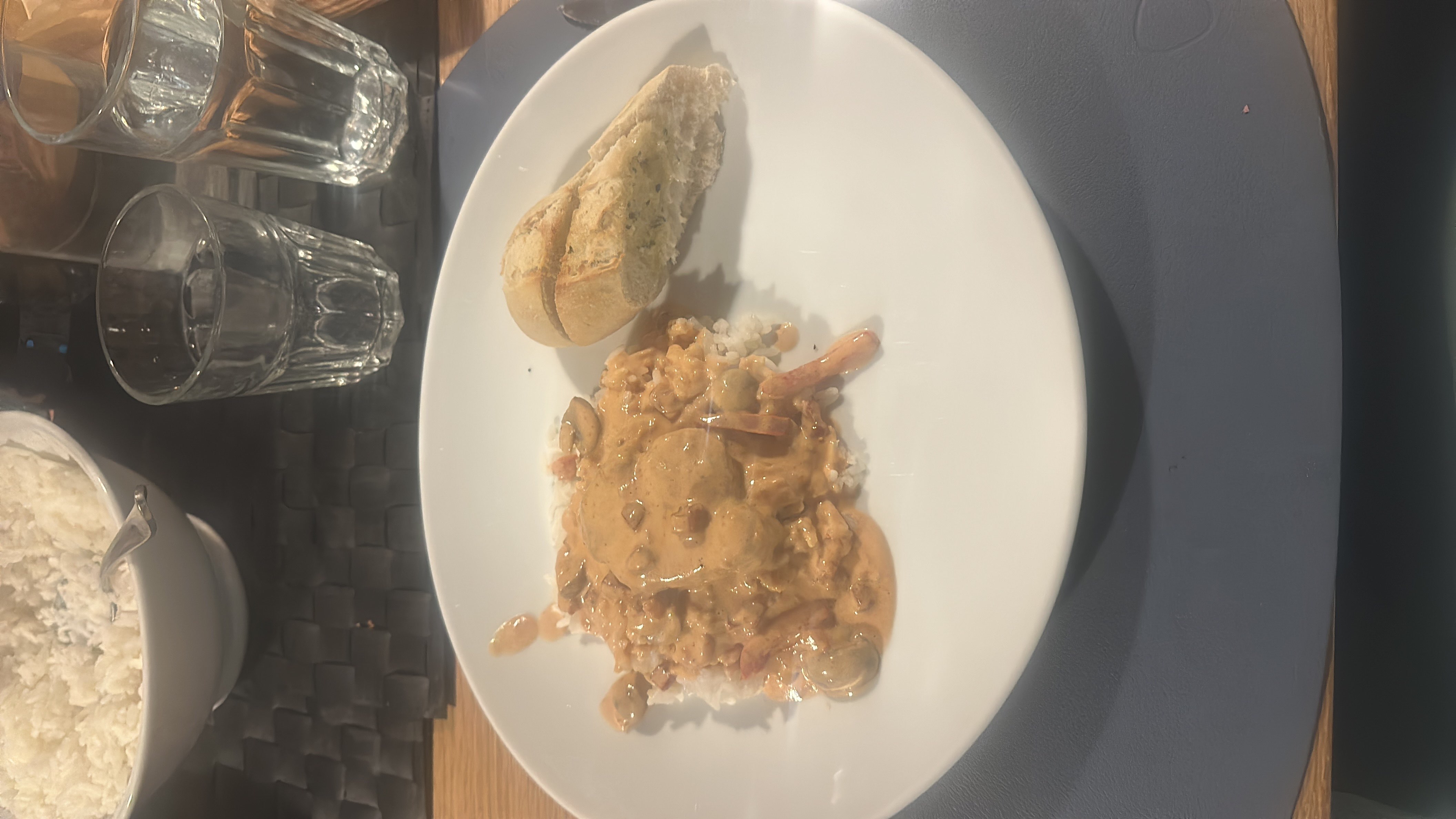 A dish consisting of rice topped with a creamy vegetable sauce and a piece of meat, served with a piece of bread.