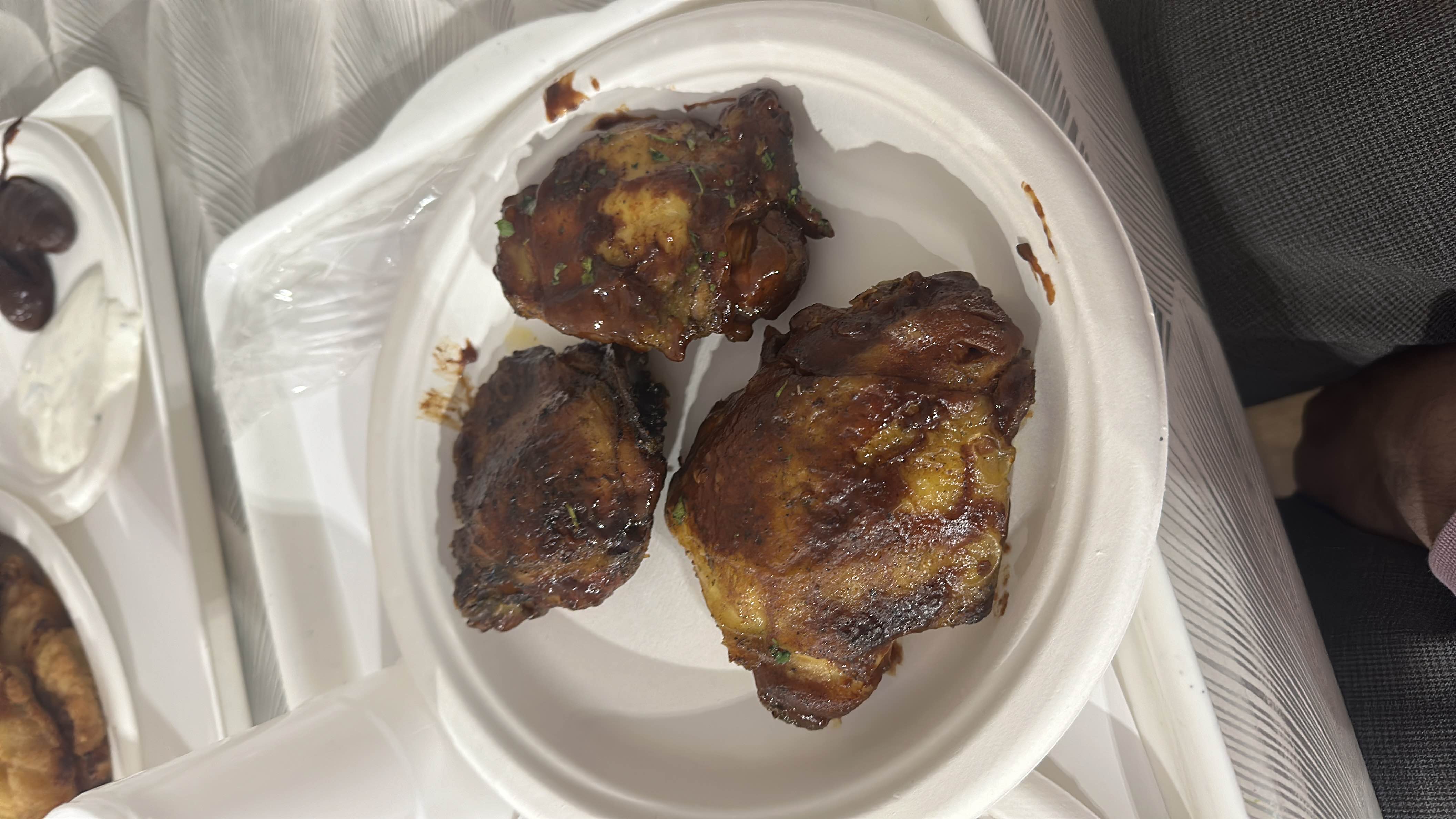 The dish consists of grilled chicken thighs coated in barbecue sauce, served on a disposable plate.
