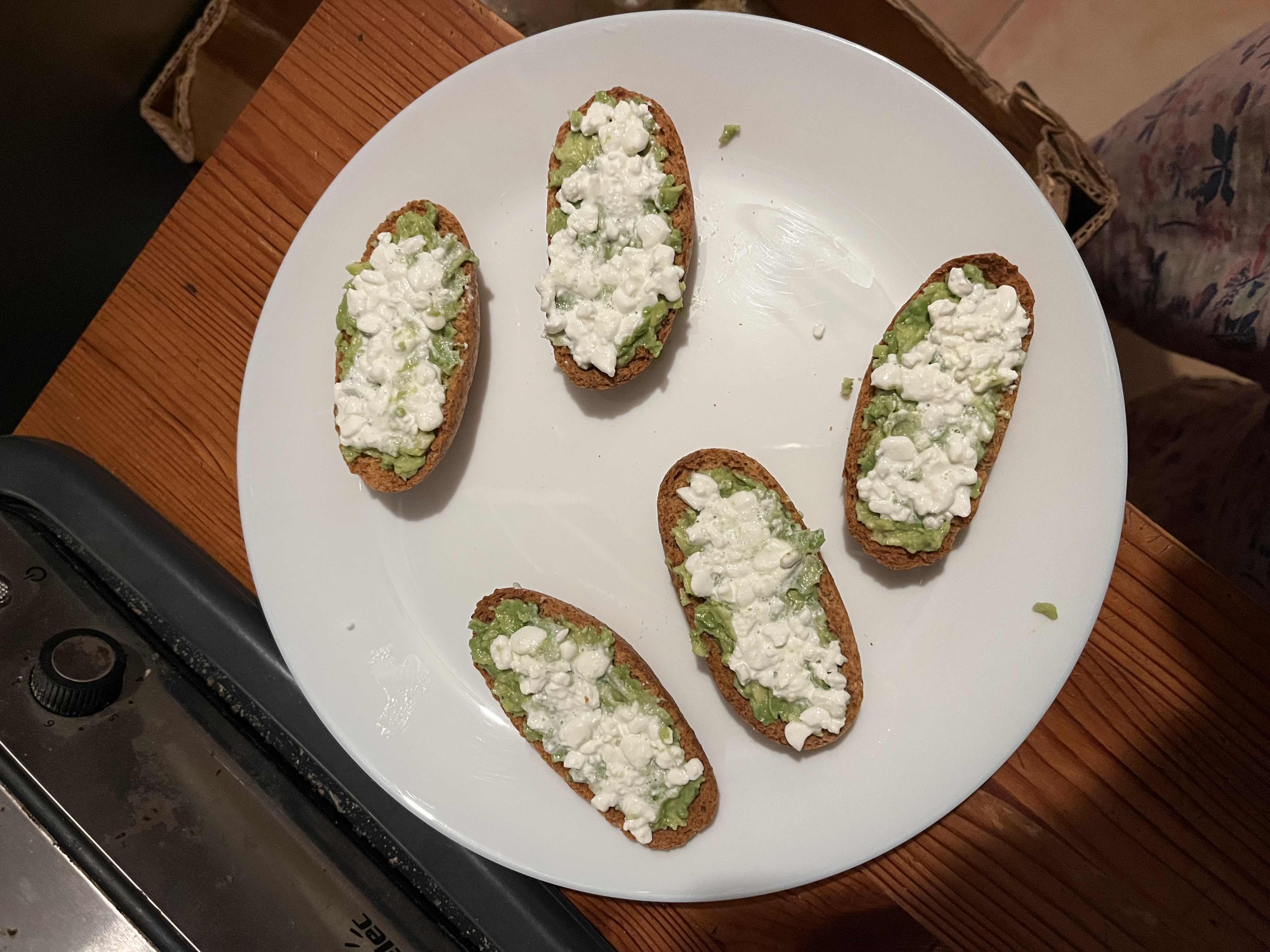 The image shows a plate of toasted bread slices topped with mashed avocado and cottage cheese, offering a balanced mix of protein, healthy fats, and carbohydrates.