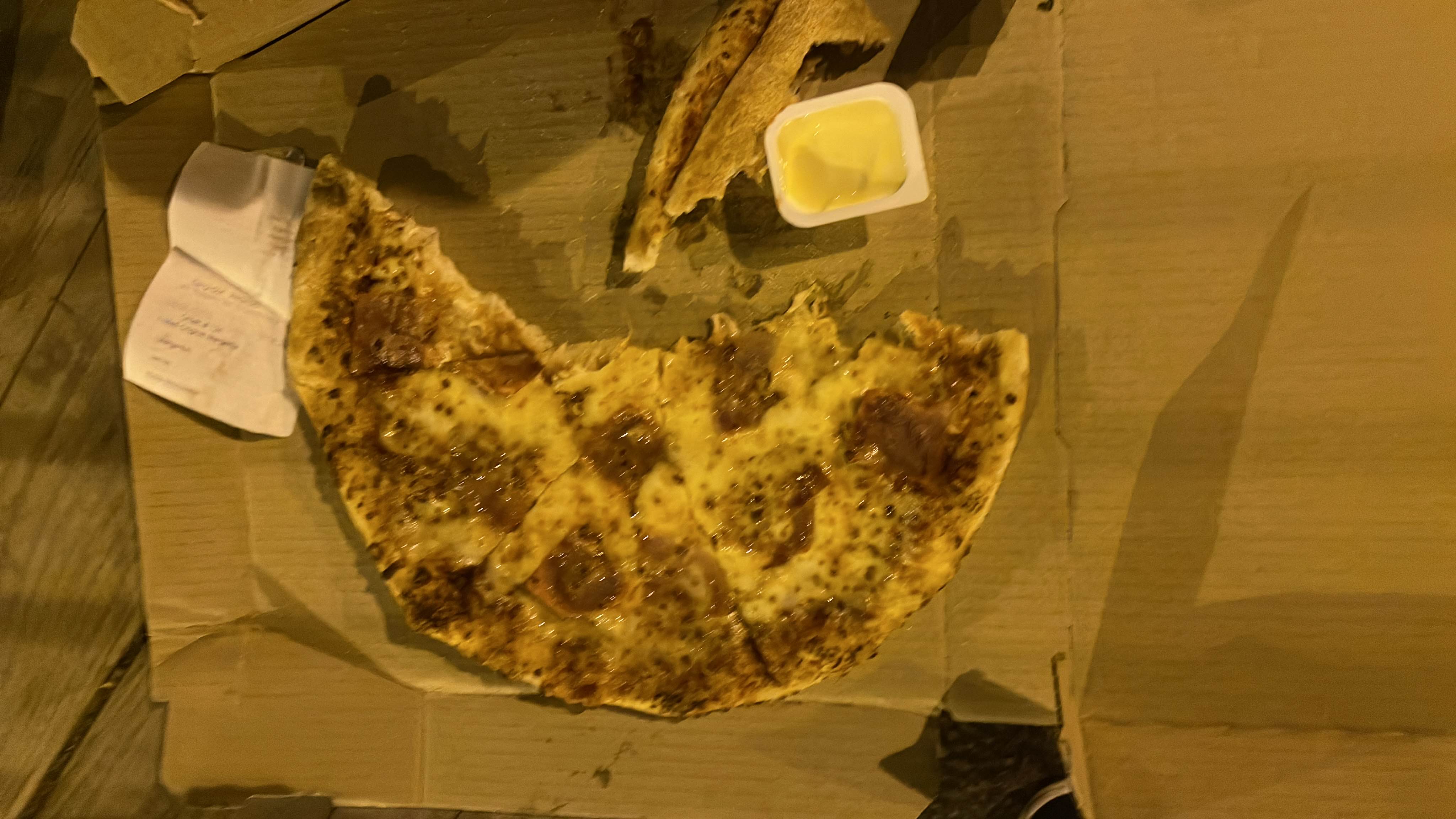 A partially eaten pepperoni pizza with cheese and a butter dip.