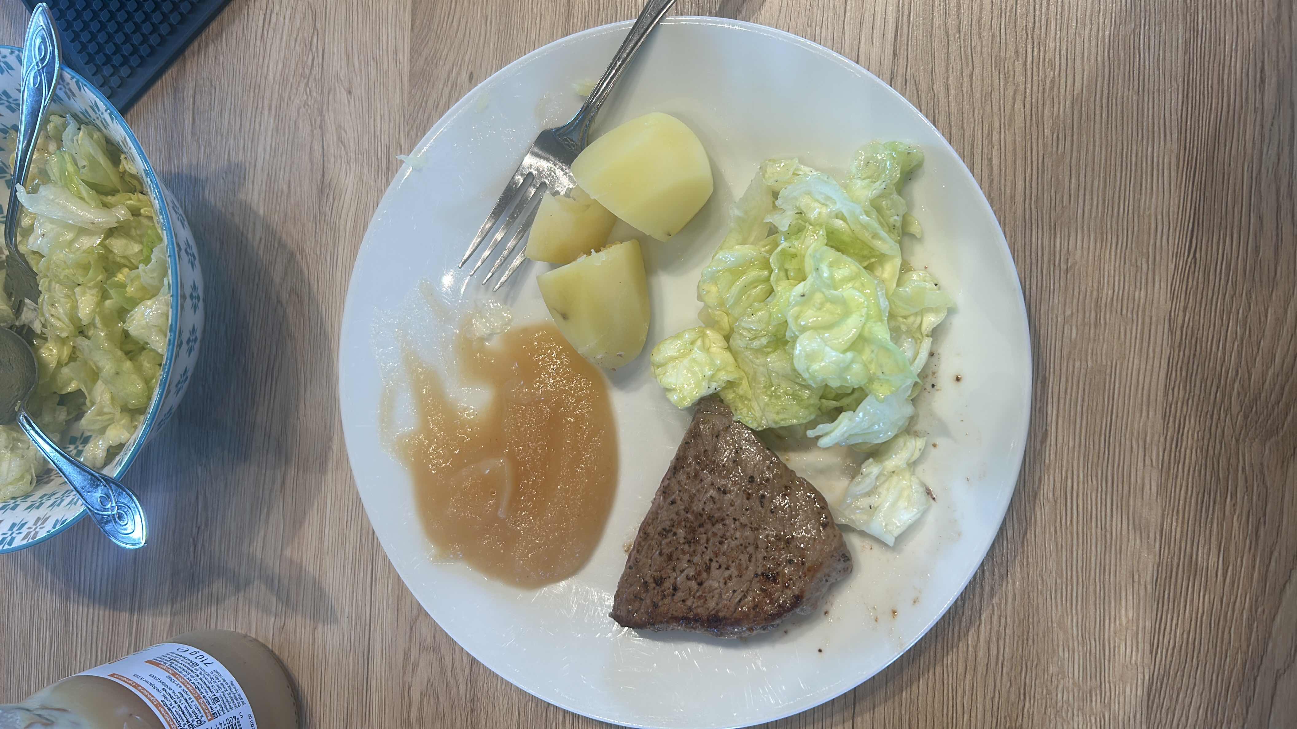 A balanced meal consisting of beef steak, boiled potatoes, lettuce salad, and apple sauce.