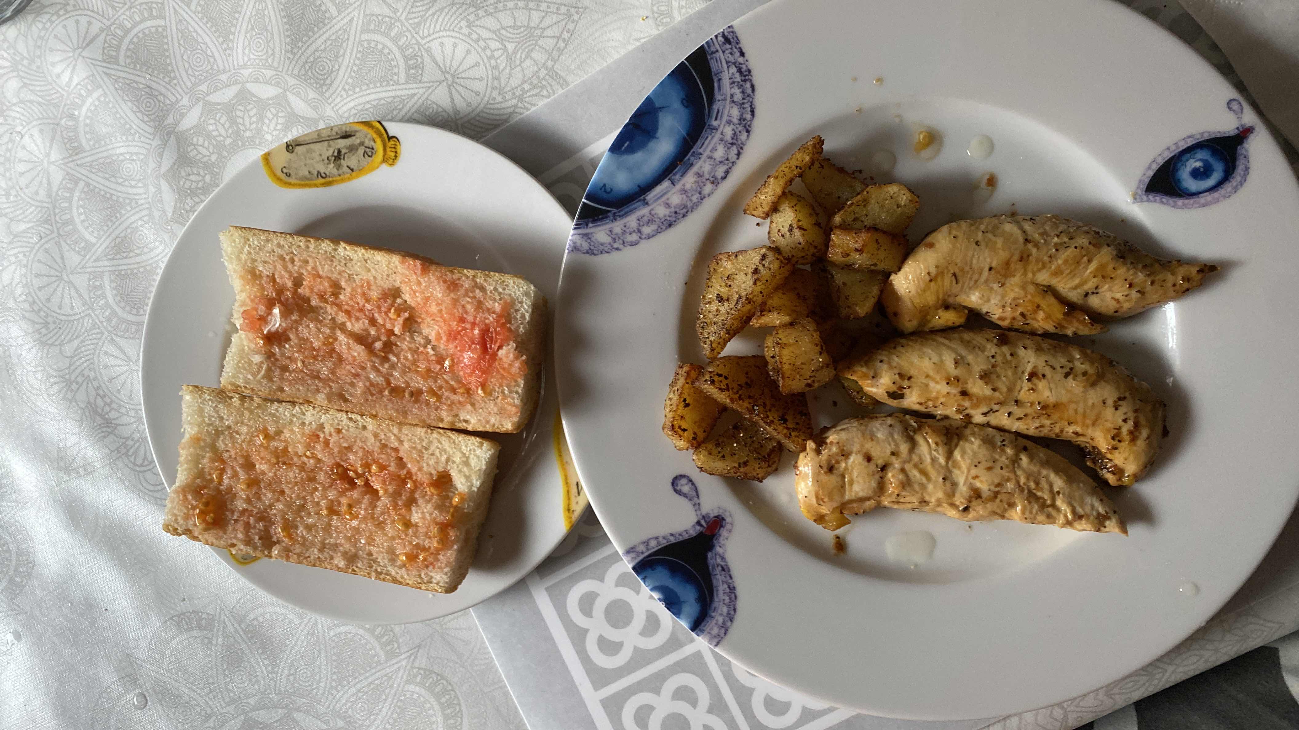 A balanced meal consisting of grilled chicken breast, seasoned potatoes, and bread with tomato spread.