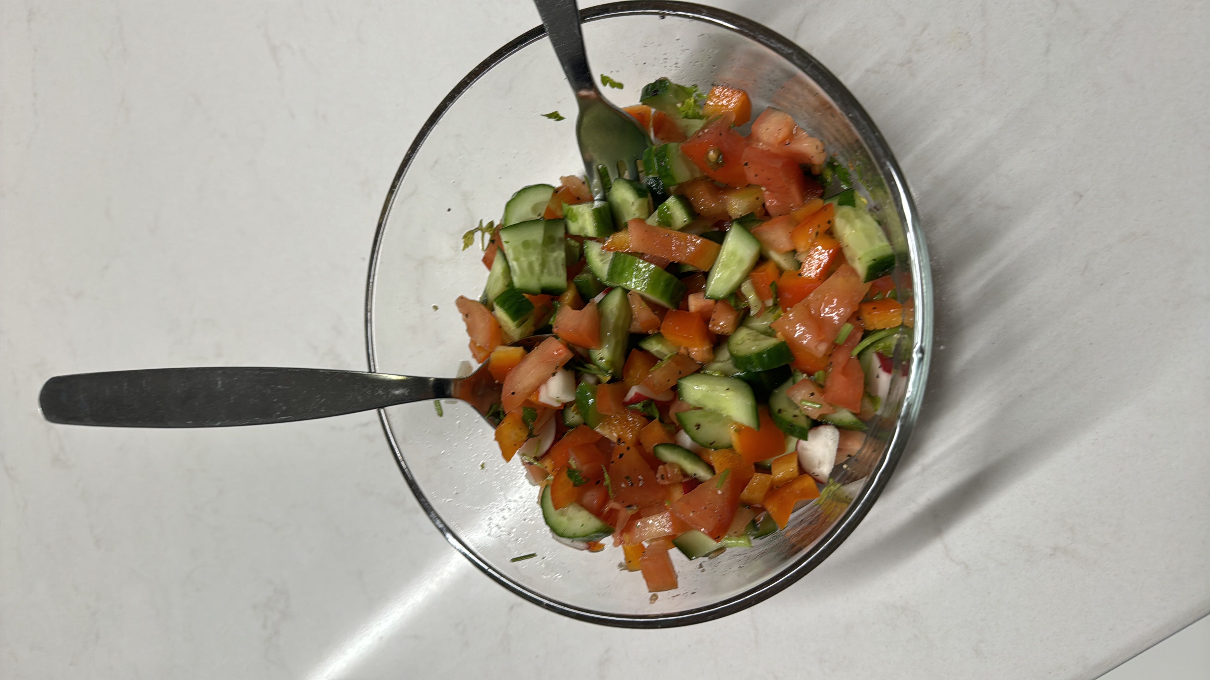 A fresh vegetable salad containing tomatoes, cucumbers, bell peppers, onions, and a drizzle of olive oil.