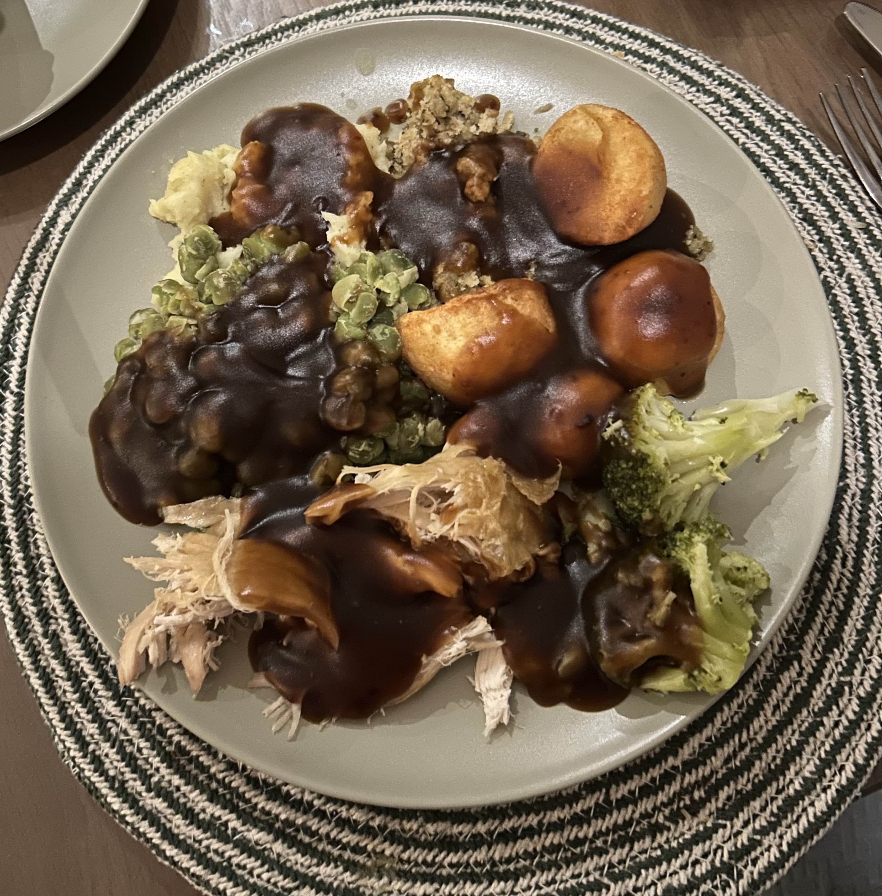 A hearty meal consisting of roast chicken, roast potatoes, broccoli, peas, stuffing, and gravy.