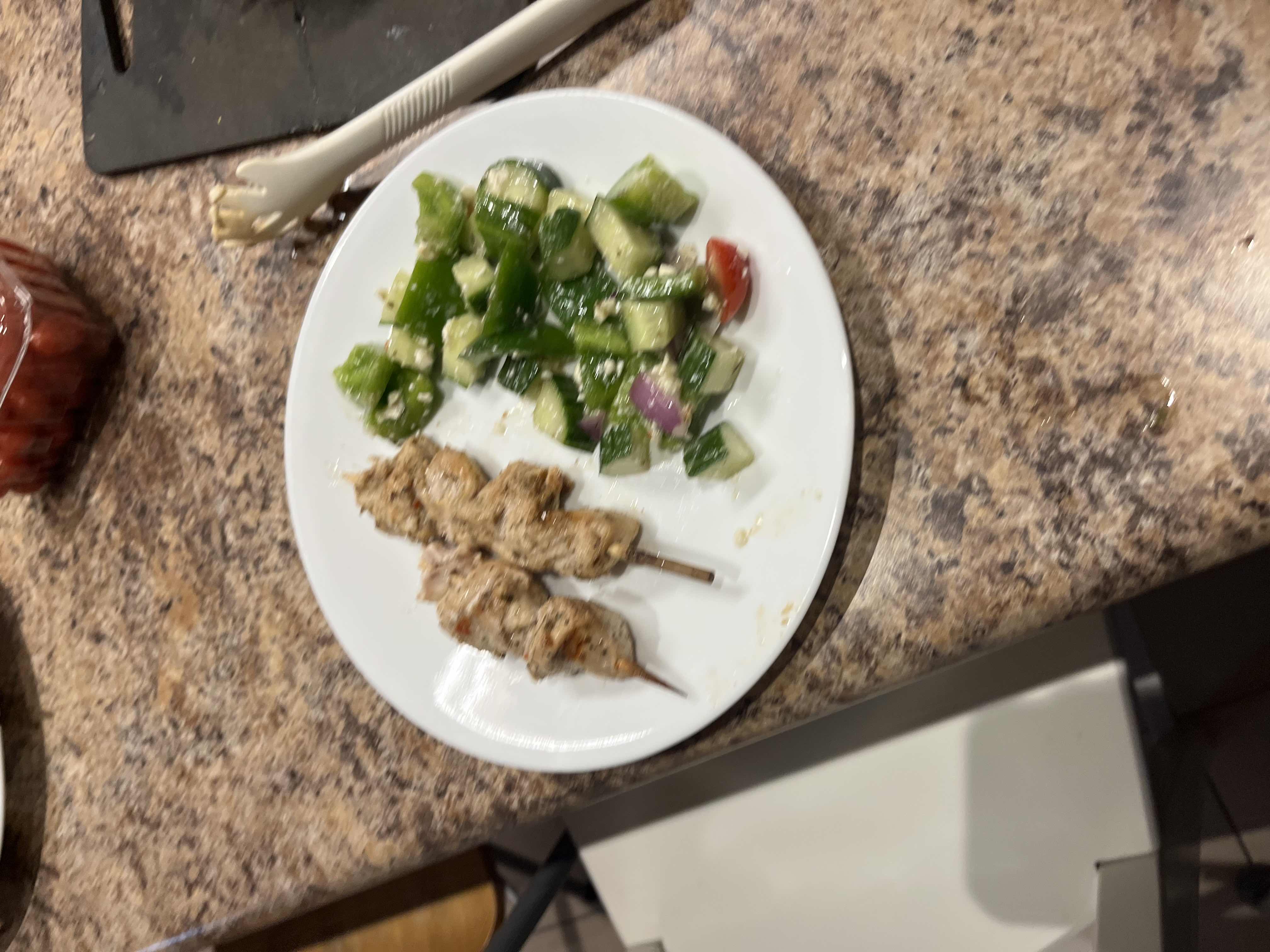 A plate containing grilled chicken skewers and a fresh vegetable salad, providing a balanced mix of protein, fats, and carbs.
