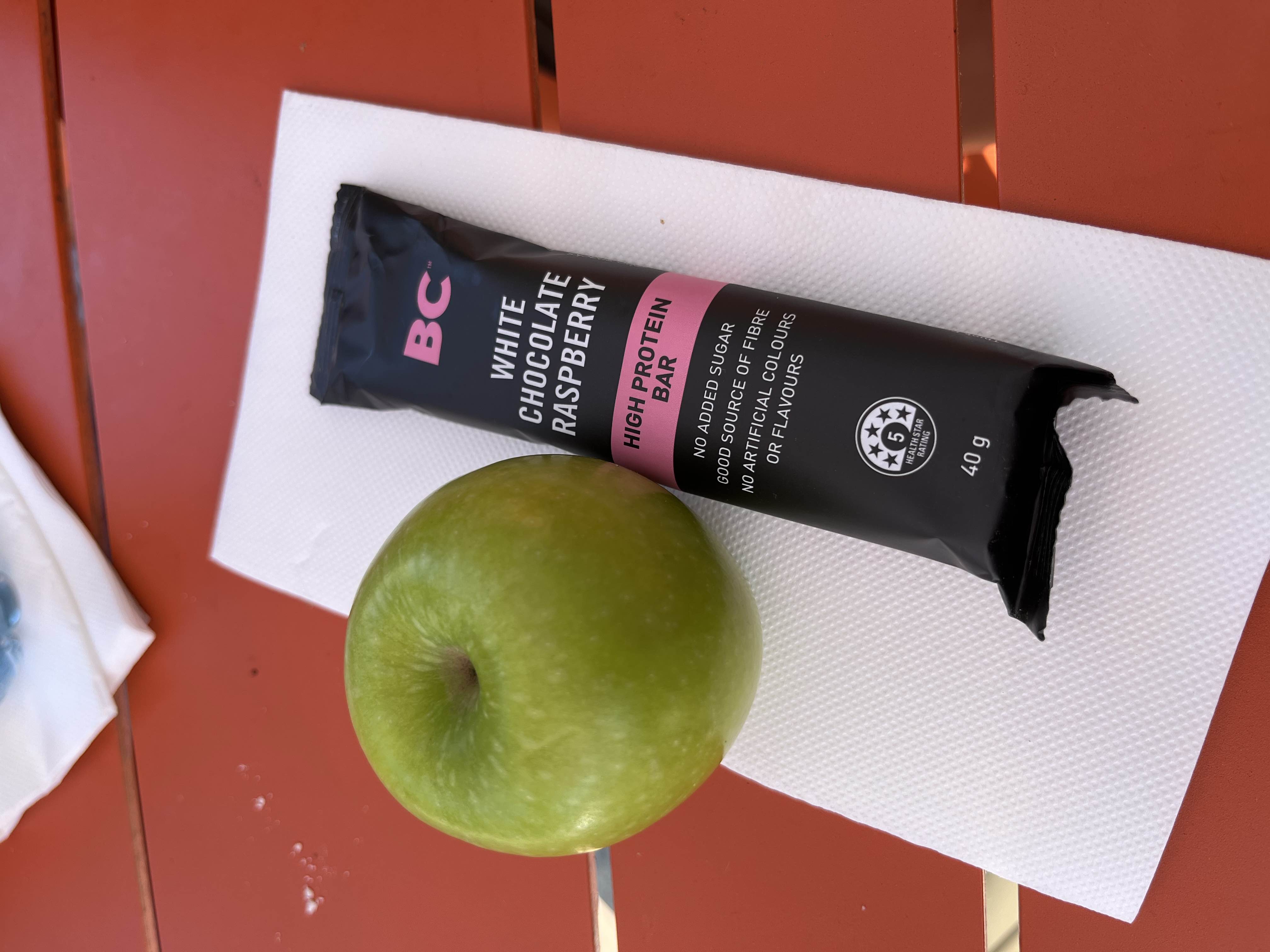 A high-protein snack consisting of a green apple and a white chocolate raspberry protein bar, providing a balanced mix of nutrients.