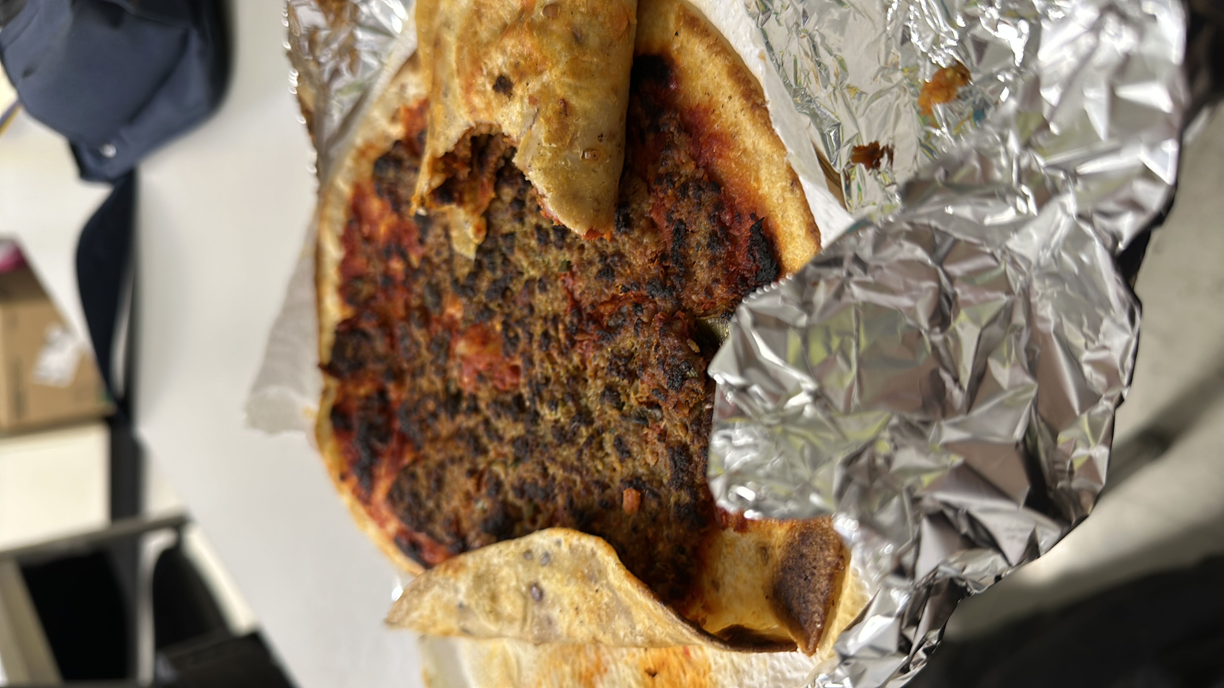 A flatbread dish topped with minced meat, tomato sauce, and spices, wrapped in foil.