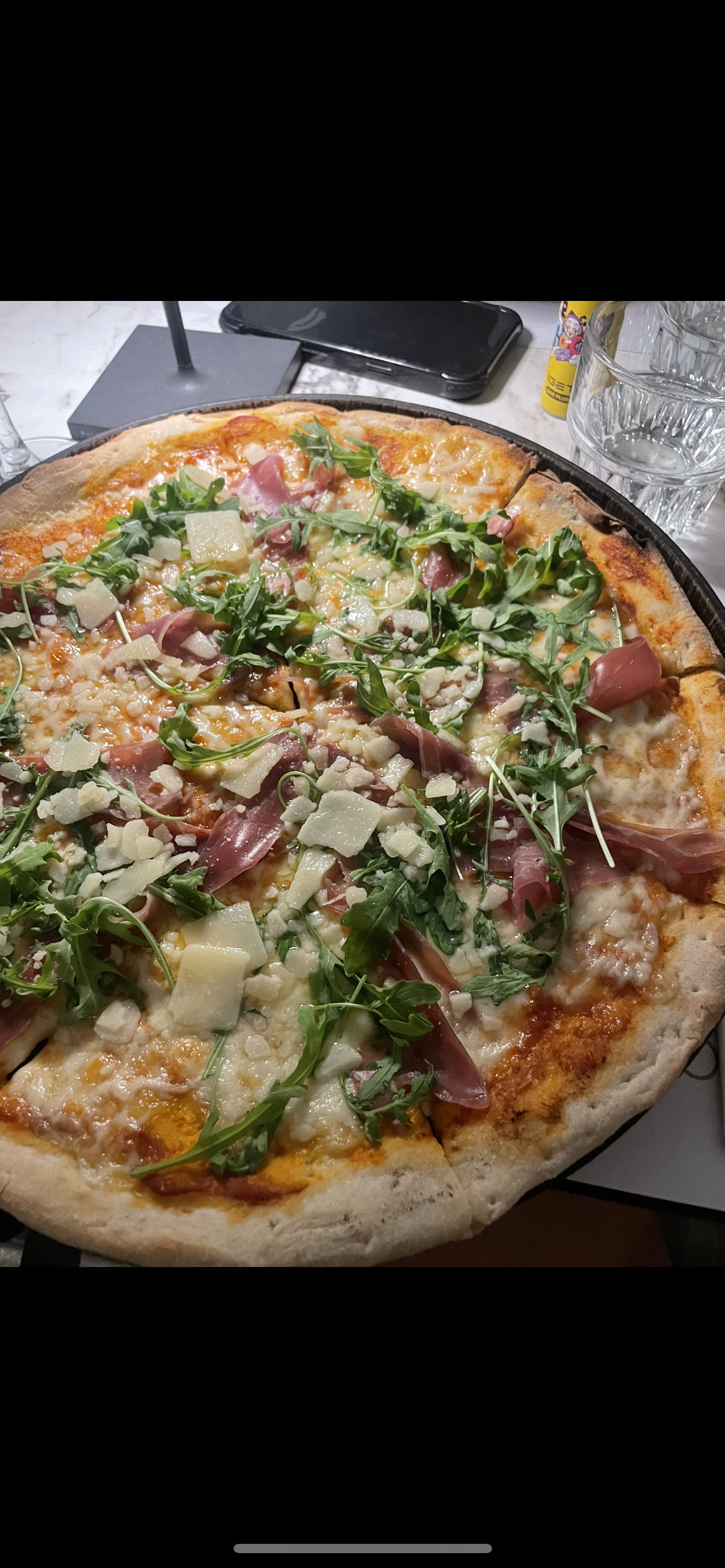 A freshly baked pizza topped with prosciutto, arugula, parmesan, cheese, and tomato sauce, offering a balanced mix of protein, carbs, and fats.