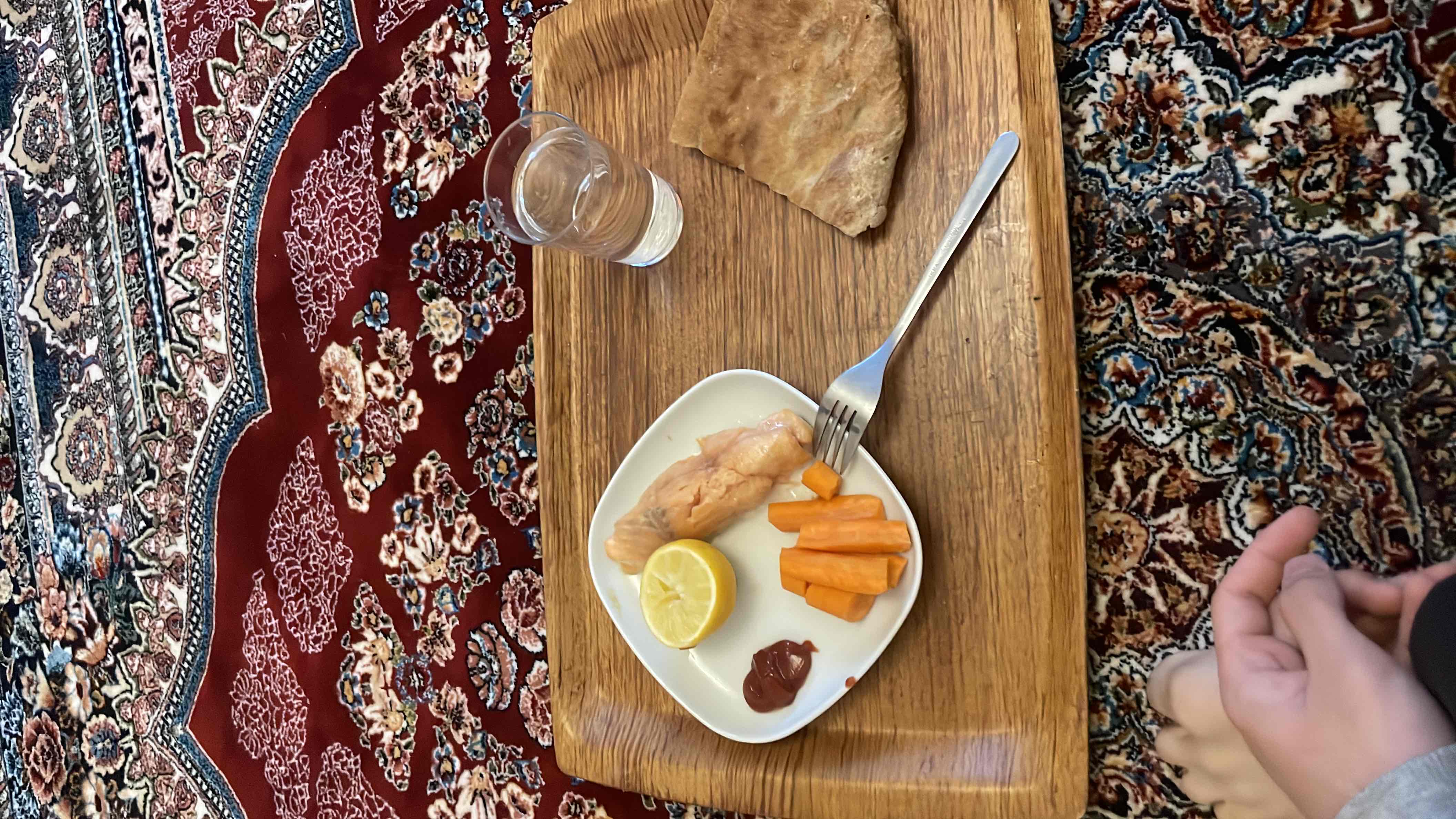 A balanced meal consisting of salmon, carrots, flatbread, and a small serving of ketchup, accompanied by a glass of water.