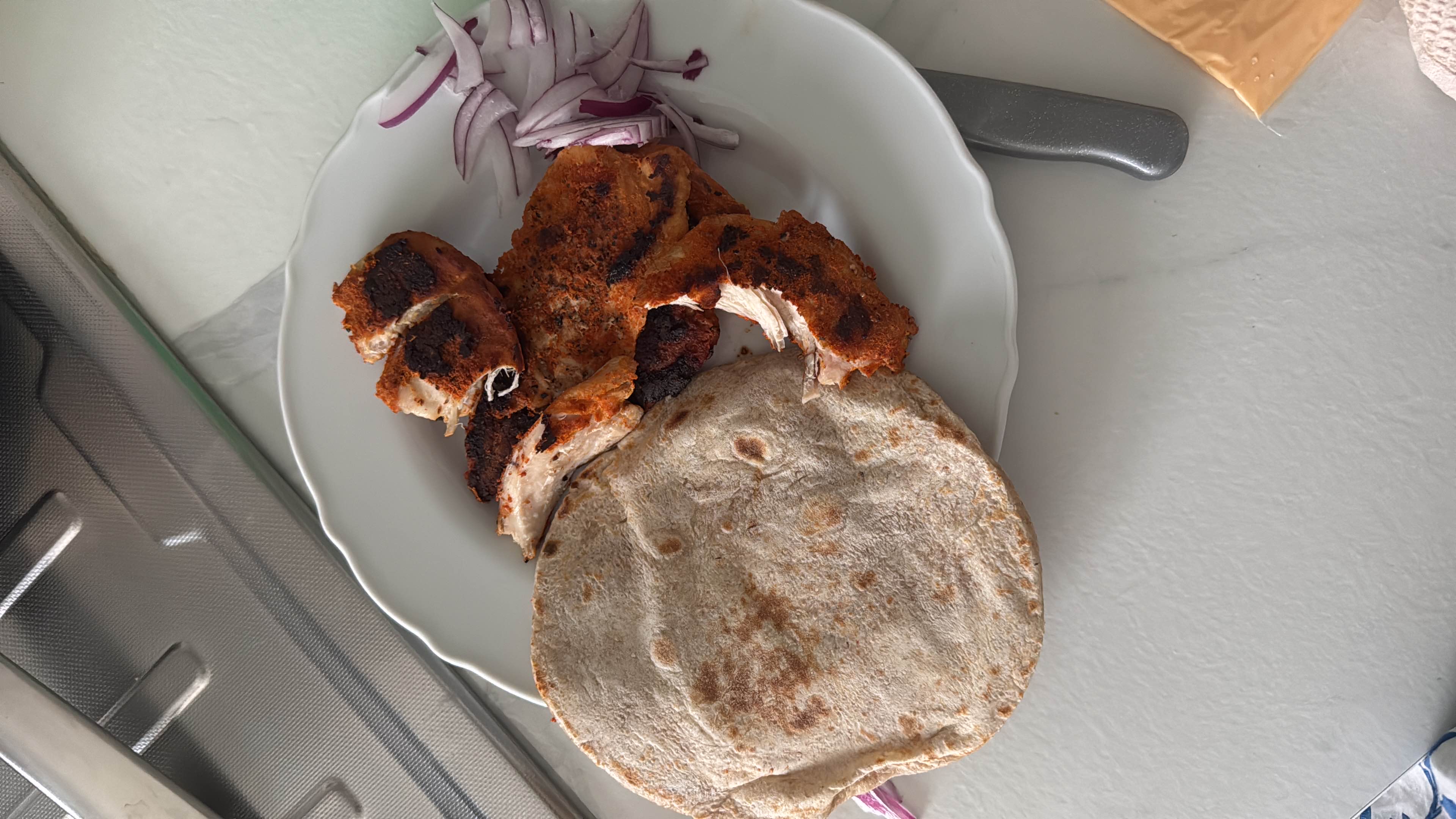 A plate containing grilled chicken, a whole wheat tortilla, and sliced red onions, offering a balanced meal with high protein and moderate carbs.