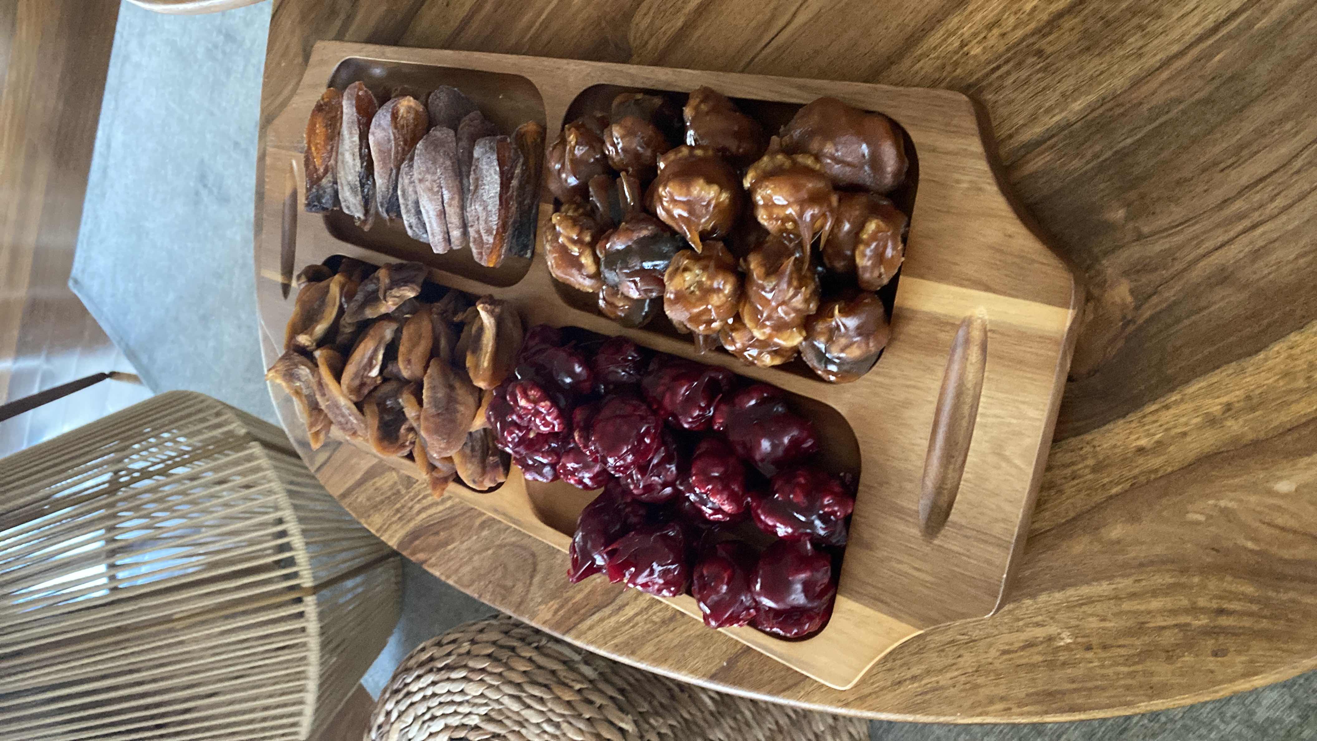 A wooden tray containing a variety of dried fruits and candied nuts, offering a nutrient-dense snack option rich in natural sugars and fiber.