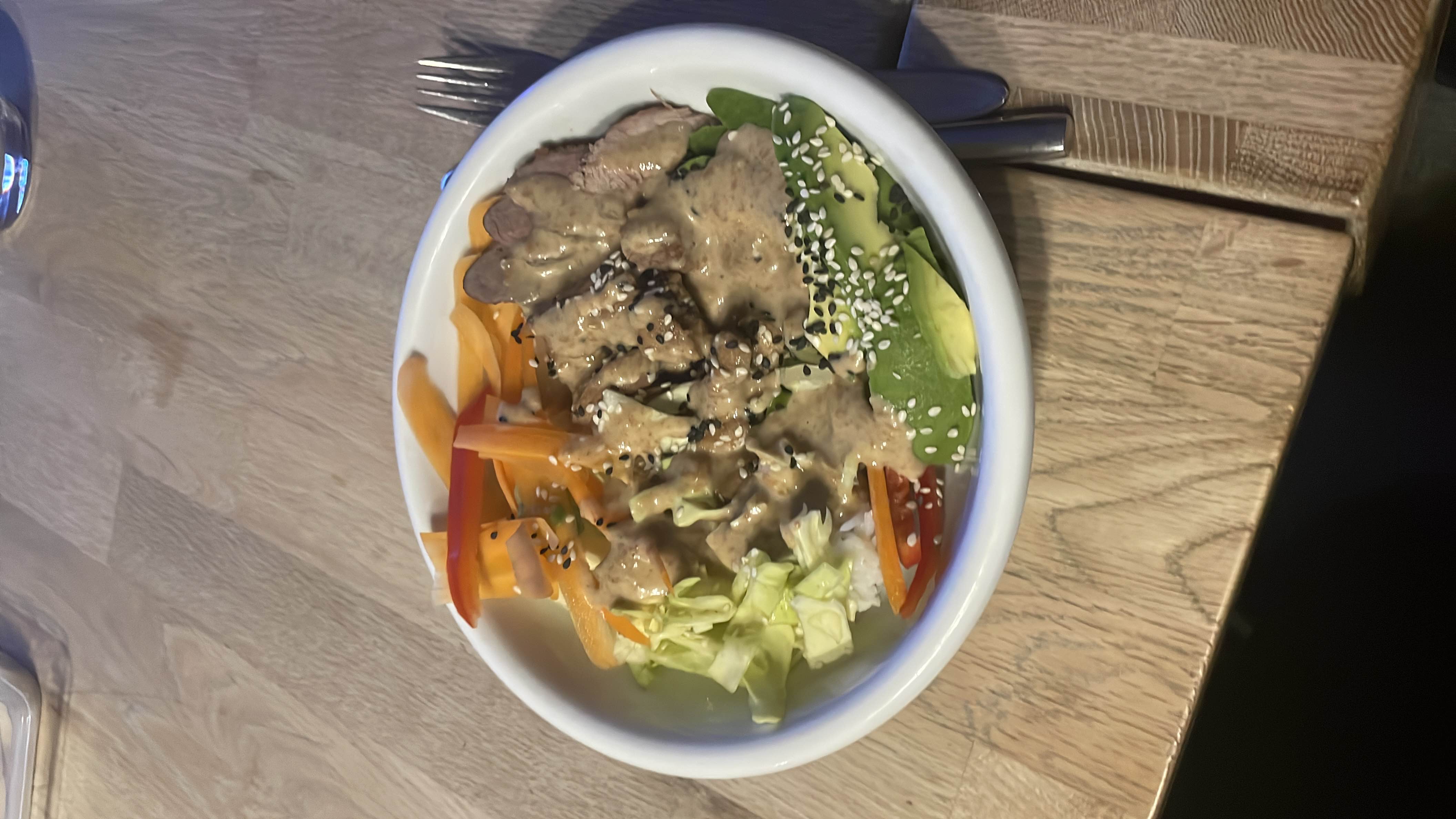 A balanced bowl containing beef slices, avocado, cabbage, carrots, sesame seeds, and a creamy dressing, offering a mix of protein, healthy fats, and vegetables.