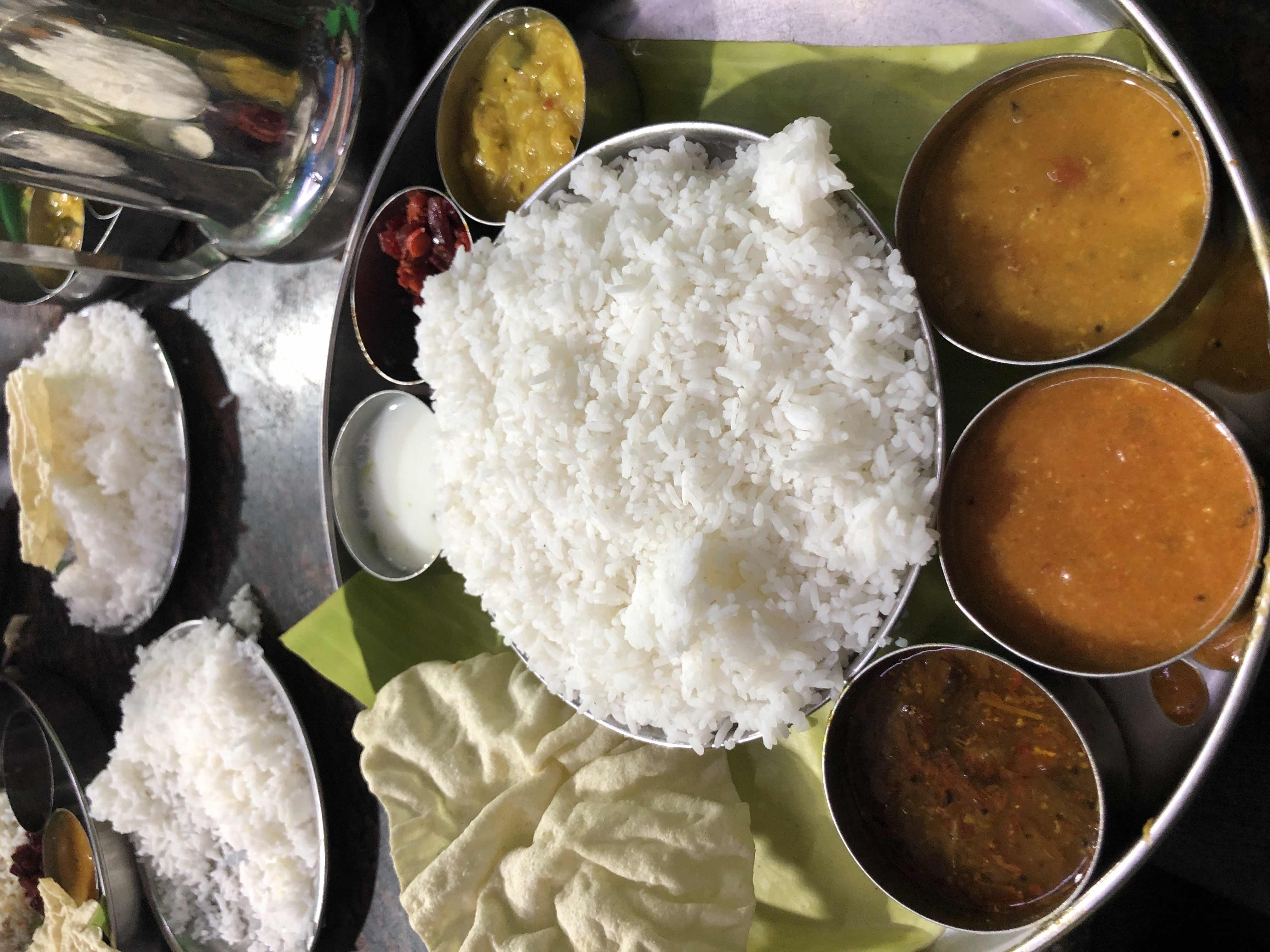 A traditional South Indian meal served on a banana leaf with rice, dal, sambar, papad, curd, and accompaniments.