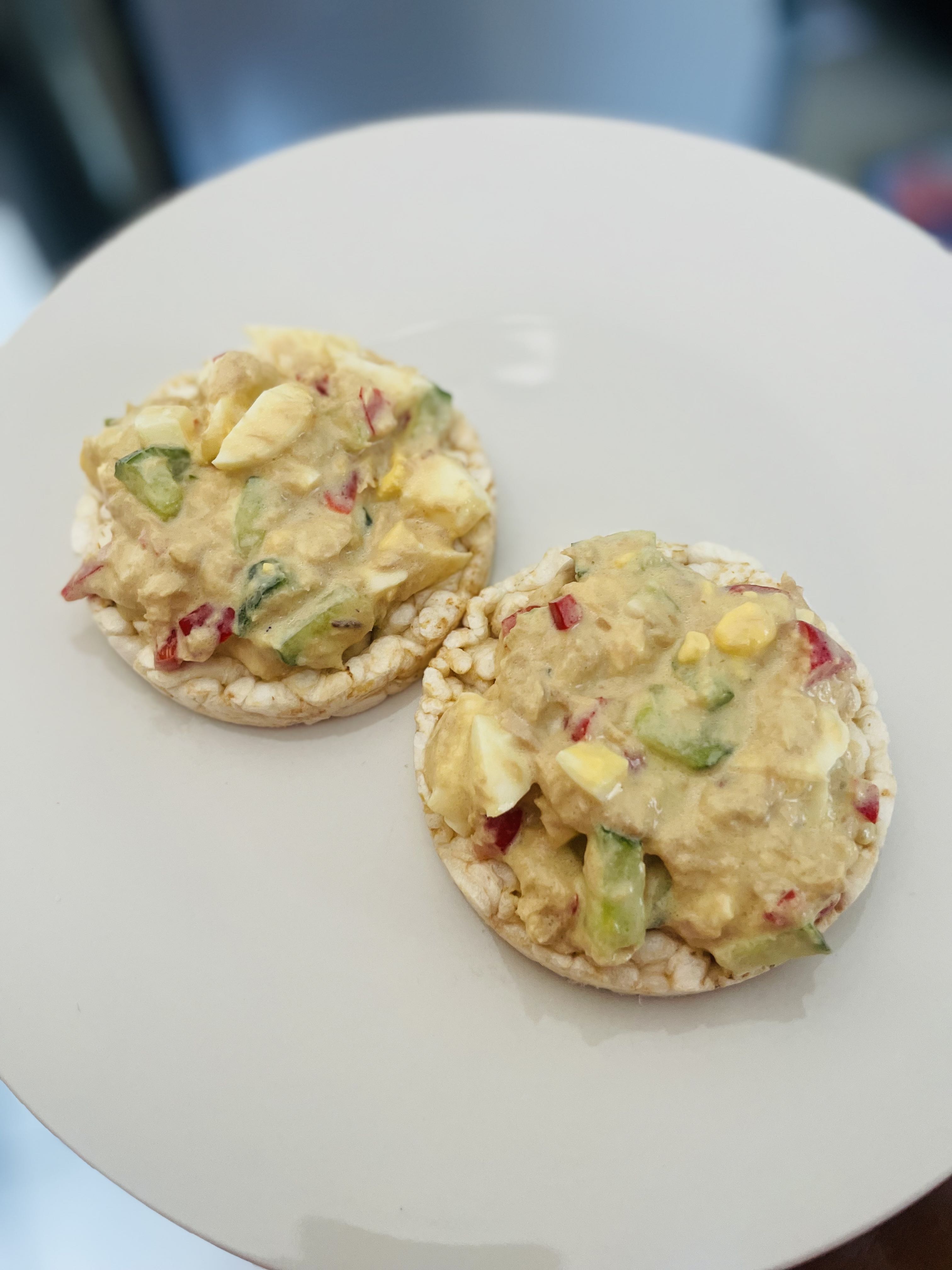 This dish consists of rice cakes topped with a mixture of tuna, boiled egg, red bell pepper, cucumber, and mayo, providing a balanced combination of protein, healthy fats, and carbohydrates.