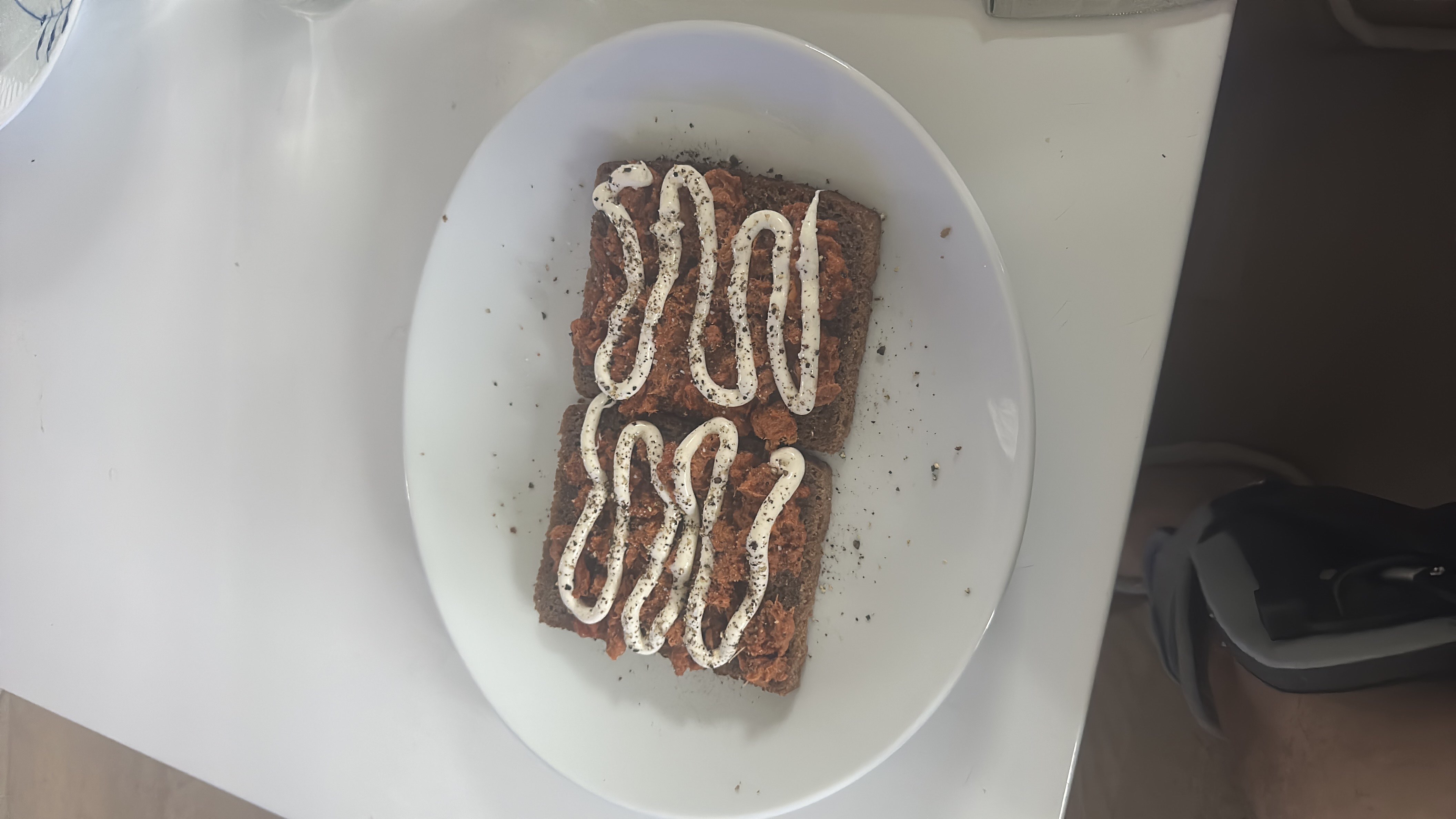 A dish consisting of rye bread topped with mackerel, mayonnaise, and a sprinkle of black pepper.