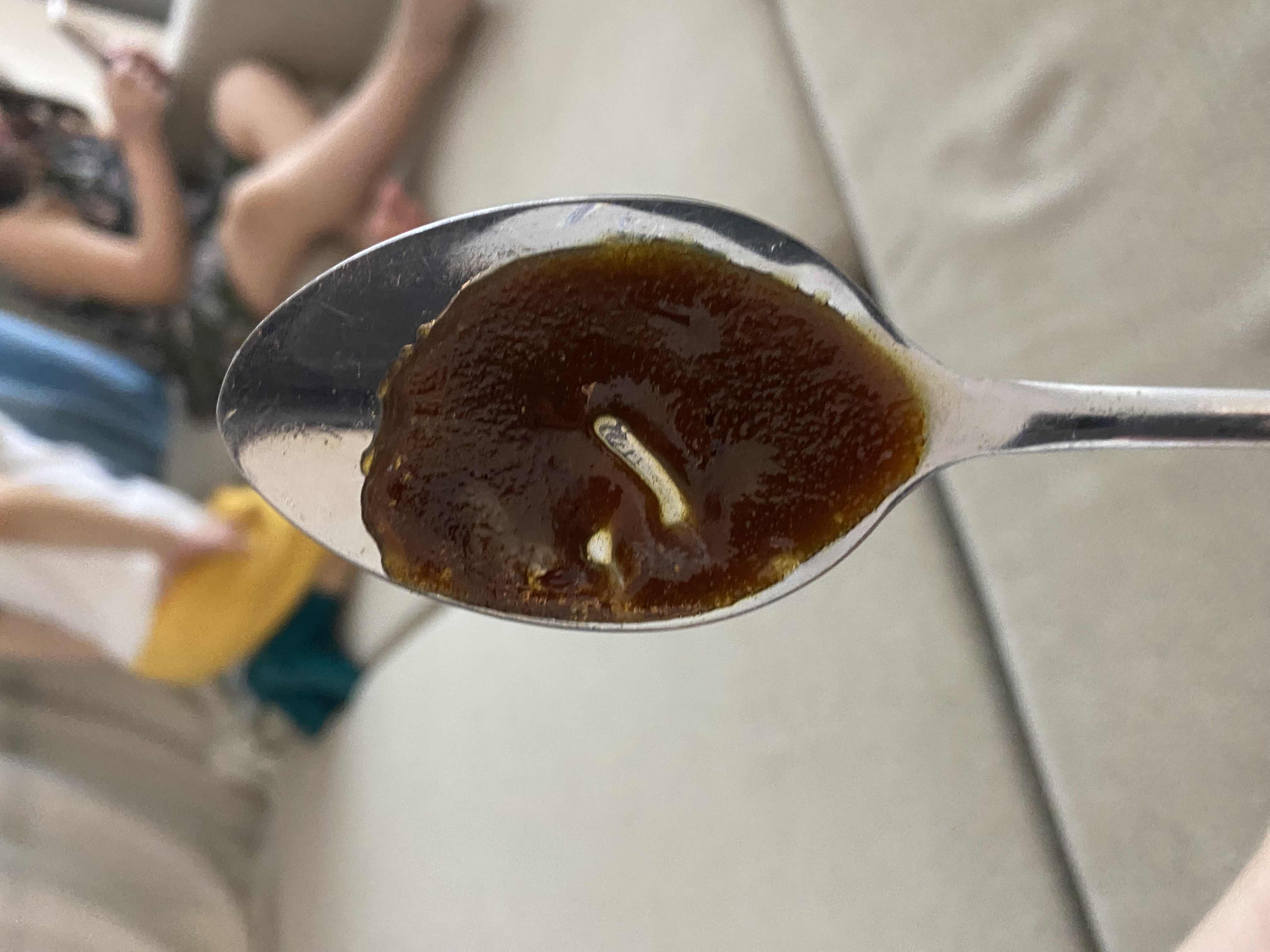 A spoonful of syrup, likely high in sugar and carbohydrates, with minimal protein and fats.