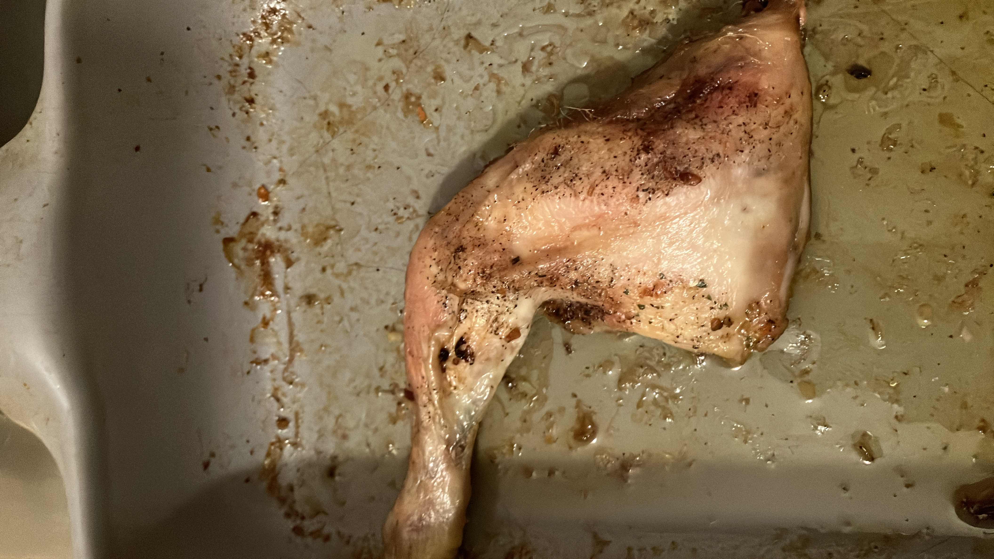 A roasted chicken leg seasoned with herbs and spices, served in a baking dish.
